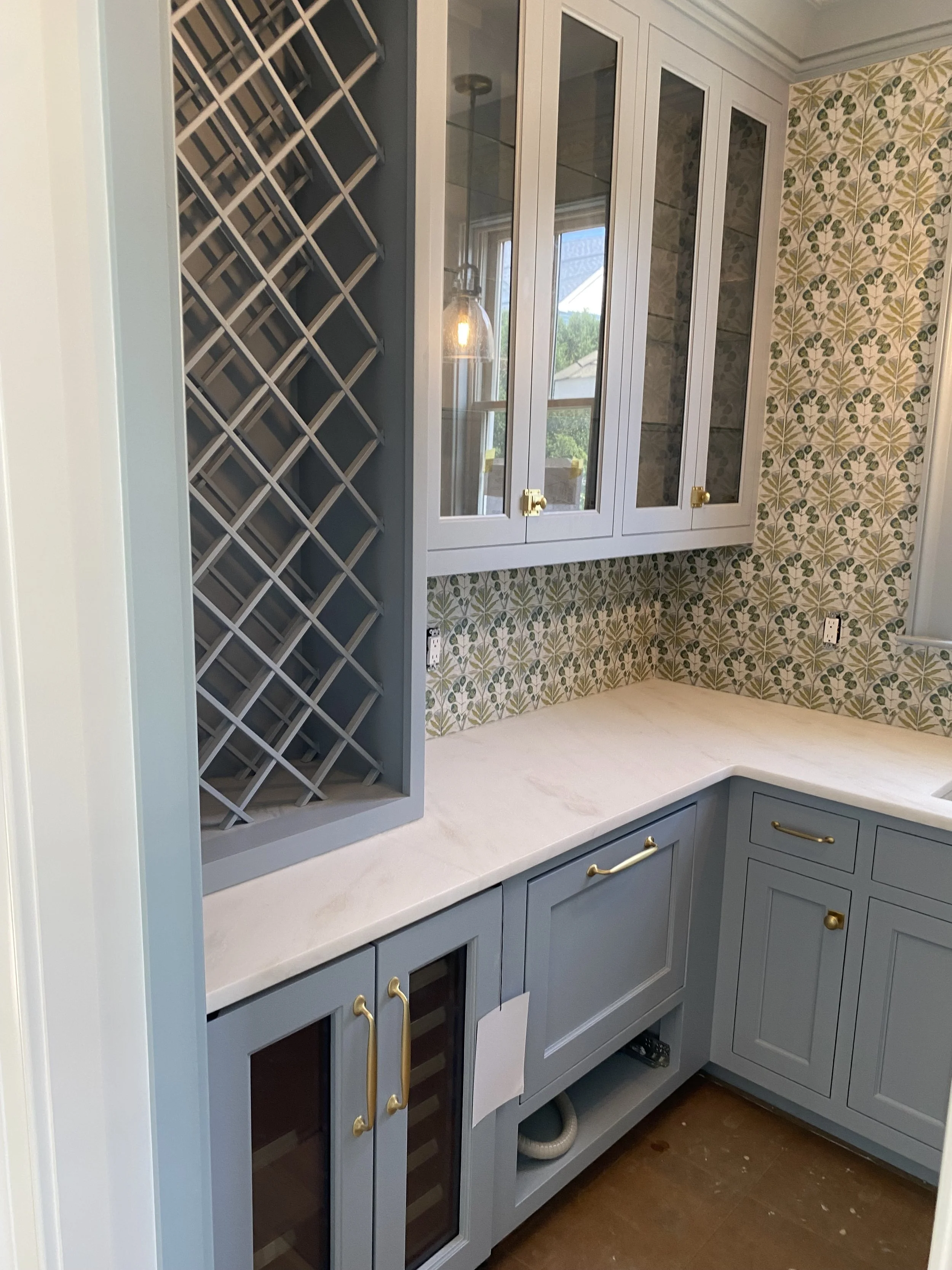 Butlers Pantry with blue cabinetry, timeless gold handles, a built-in wine rack, and a backsplash with a floral-patterned tile design. 