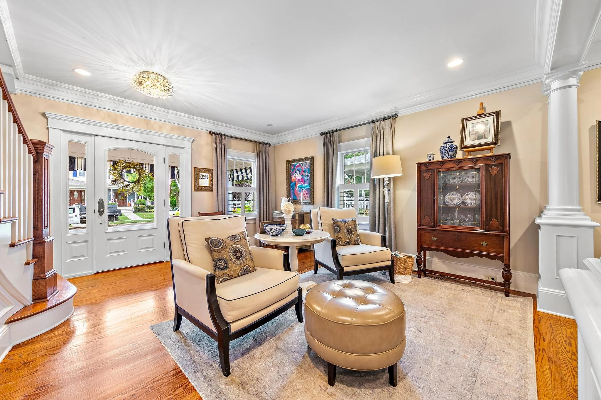 Living room with hardwood floors, two elegant armchairs with fluffy throw pillows,, and large windows with statement window treatments.