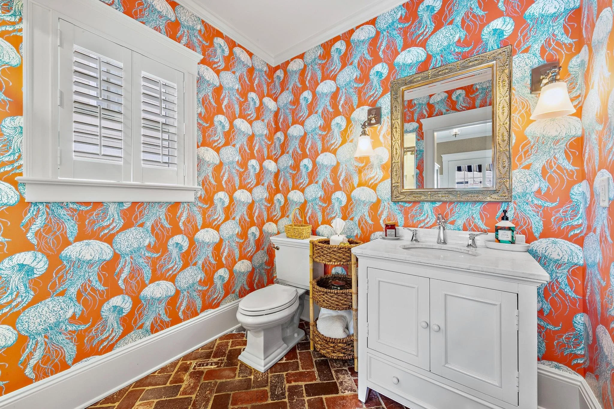 Bathroom with bold coastal wallpaper, white window shutters, a white vanity and a timeless brick floor.