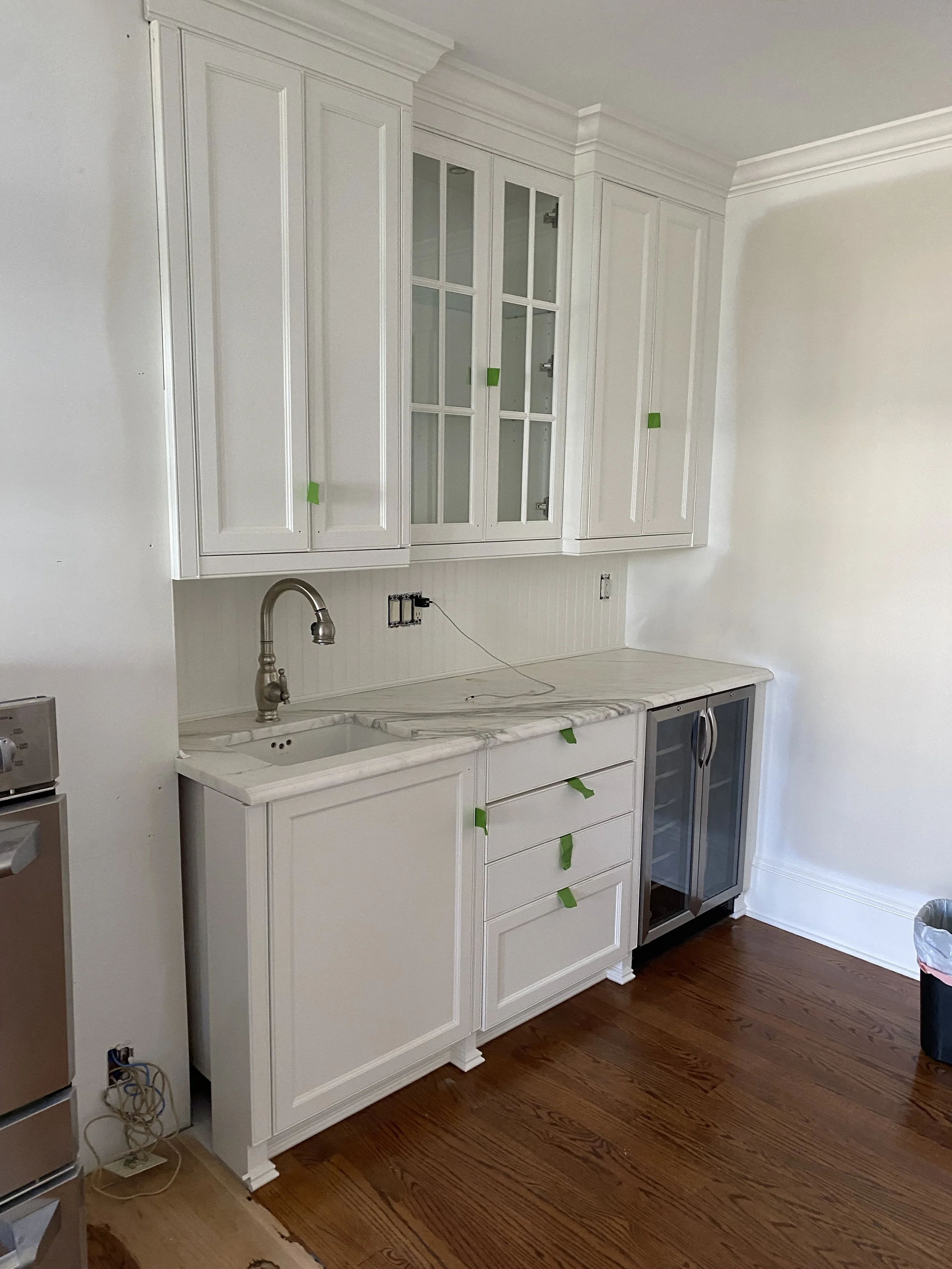 Bar area cabinetry with glass-front upper cabinets, marble countertop, stainless steel sink, and wine fridge, with hardwood flooring.