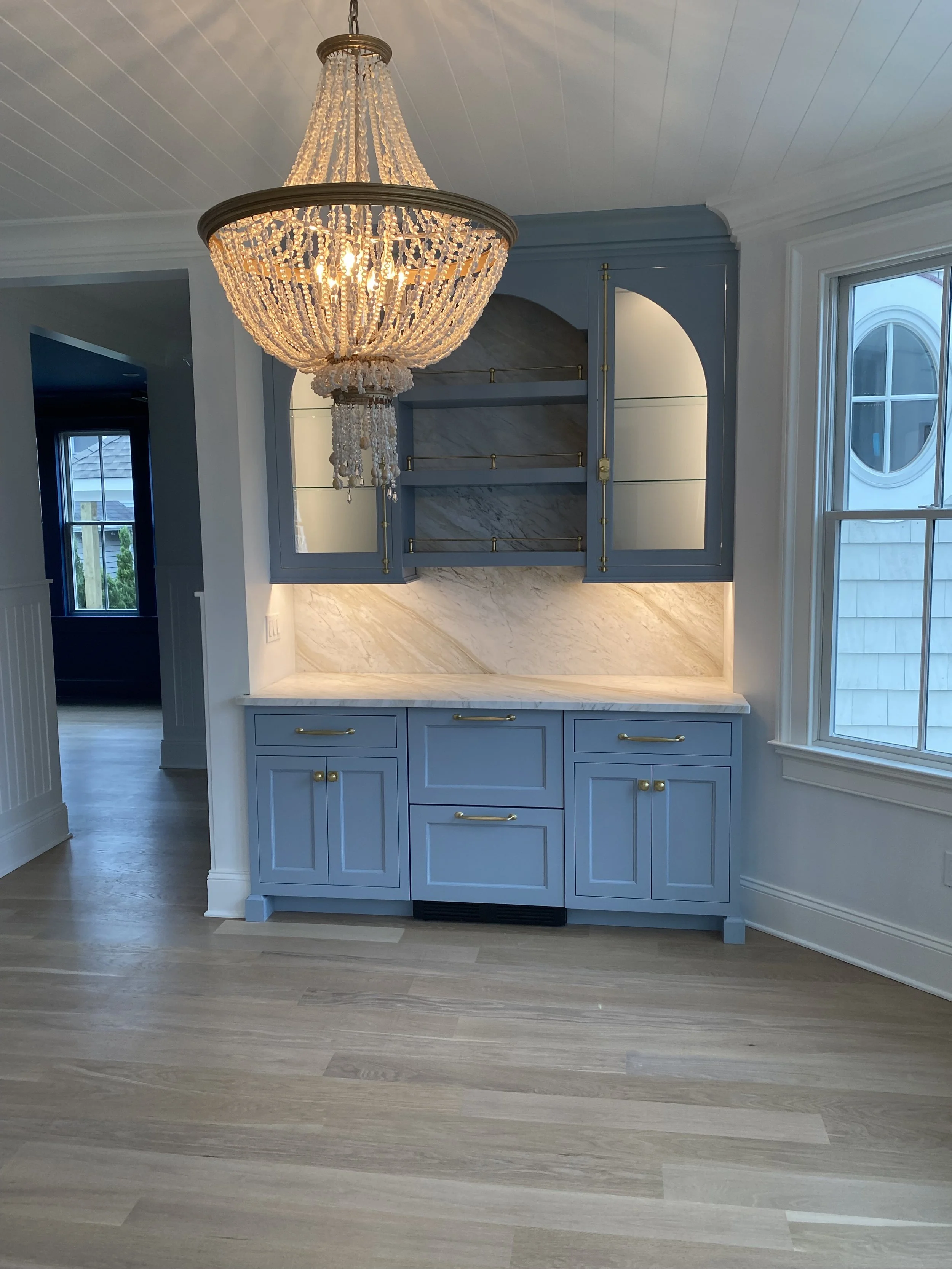 A dining area with a relaxing blue cabinet featuring timeless gold hardware, a marble countertop and backsplash. 