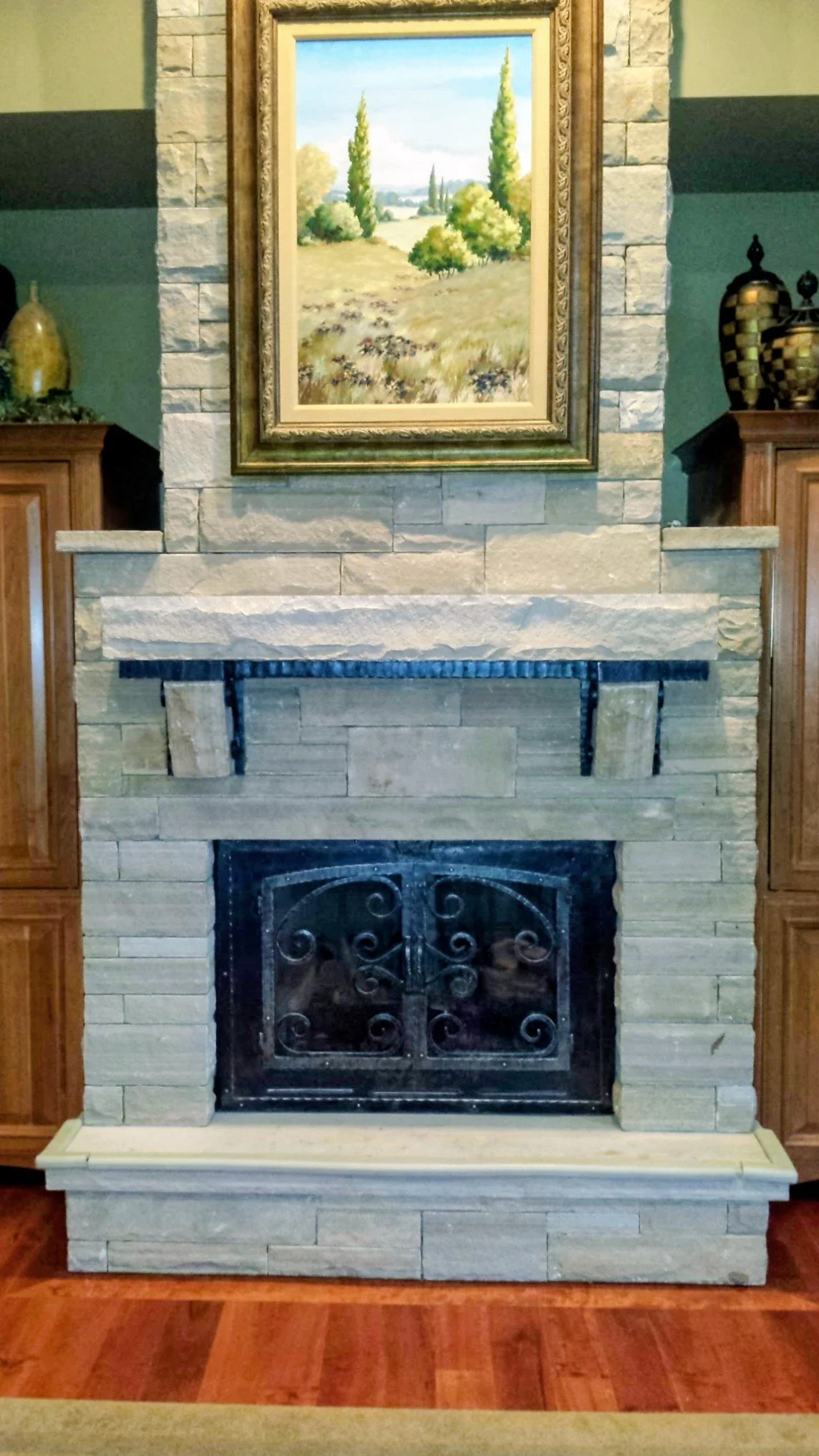 Steel fireplace mantel and wrought iron fireplace doors installed in stone surround.