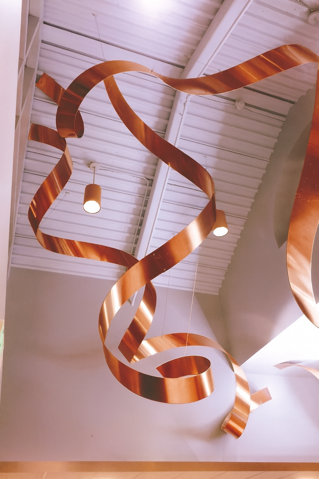 Suspended sculptural copper ribbon feature installed in commercial space.