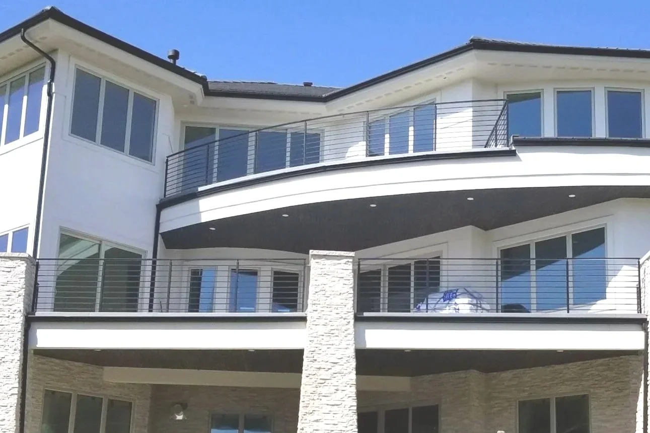 Black deck railings on large multi-story modern residential building with large windows and balconies, featuring white walls.