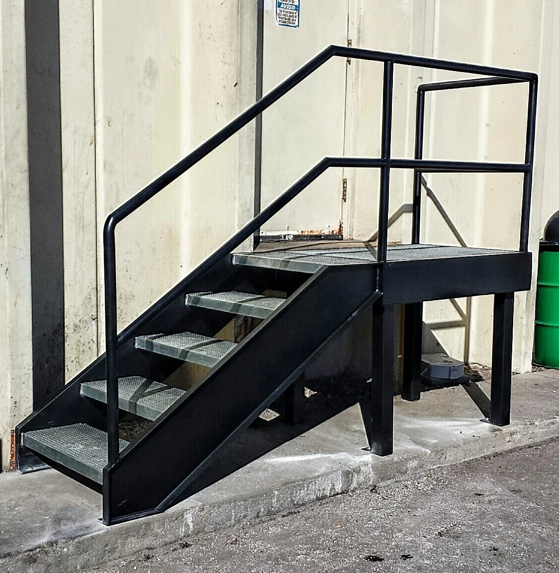 Black steel exterior access stairs with landing platform and guardrail installed against commercial building.