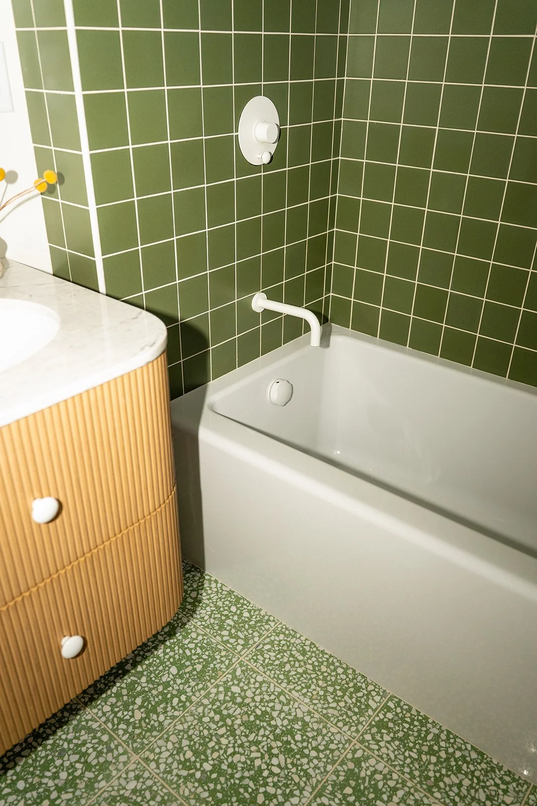 Green tiled bathroom with white bathtub, white faucet, and a small wooden cabinet with white round knobs.