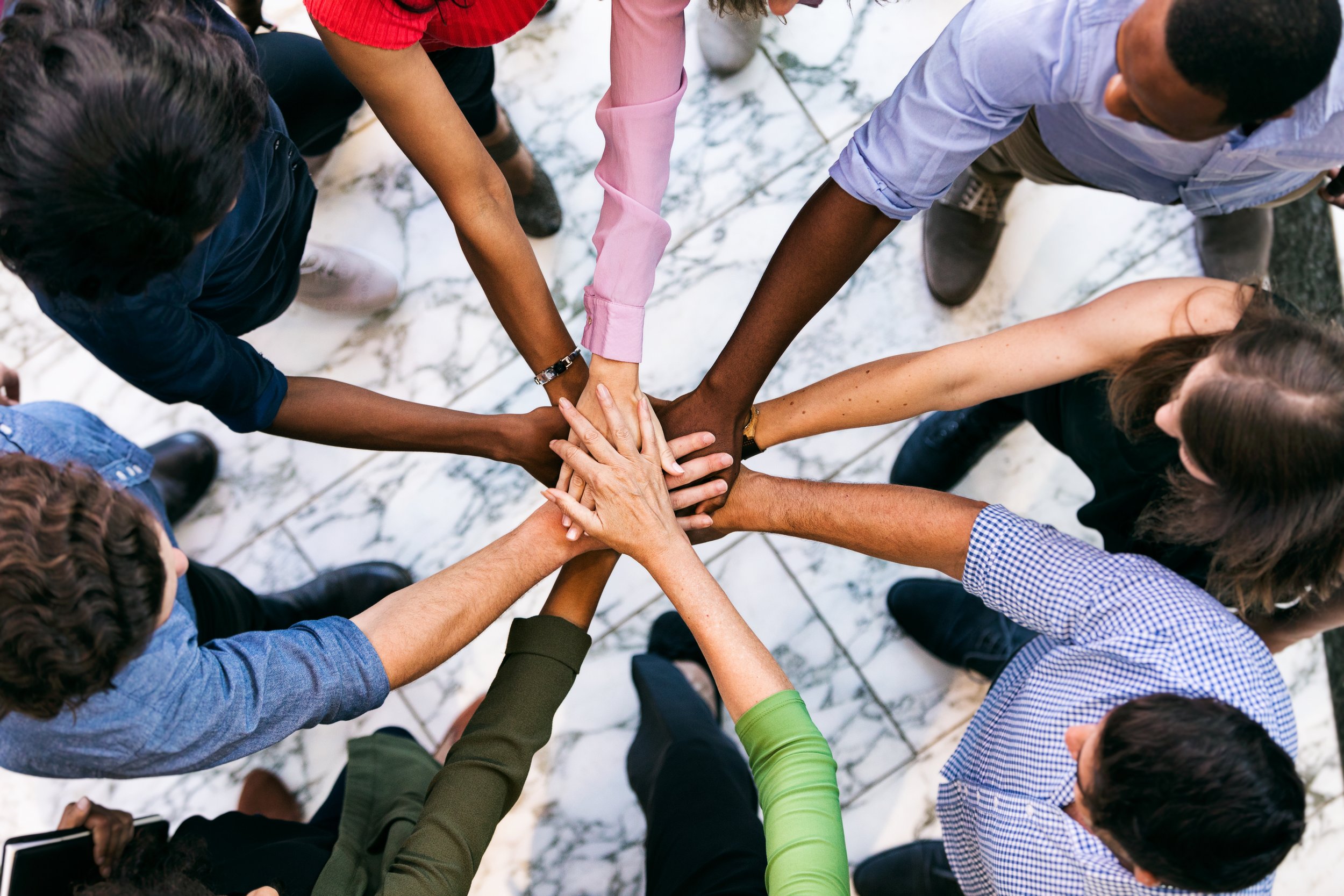 A group of speech, occupational, and physical therapists in Houston, TX wearing diverse clothing placing their hands together in a circle, symbolizing teamwork and unity.