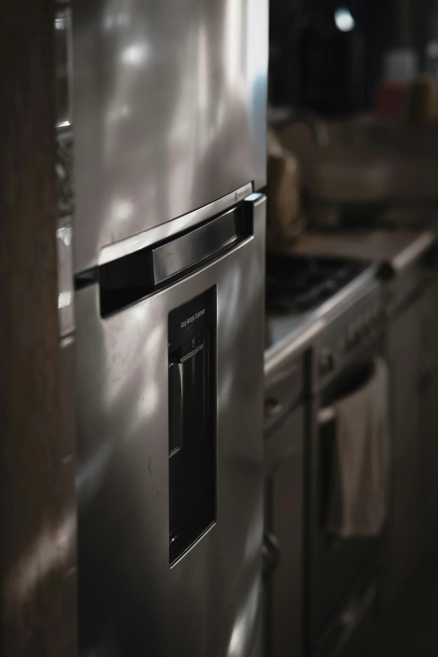 Close-up of a stainless steel refrigerator in a kitchen, with a glimpse of a stove and kitchen towel hanging on a handle in the background.