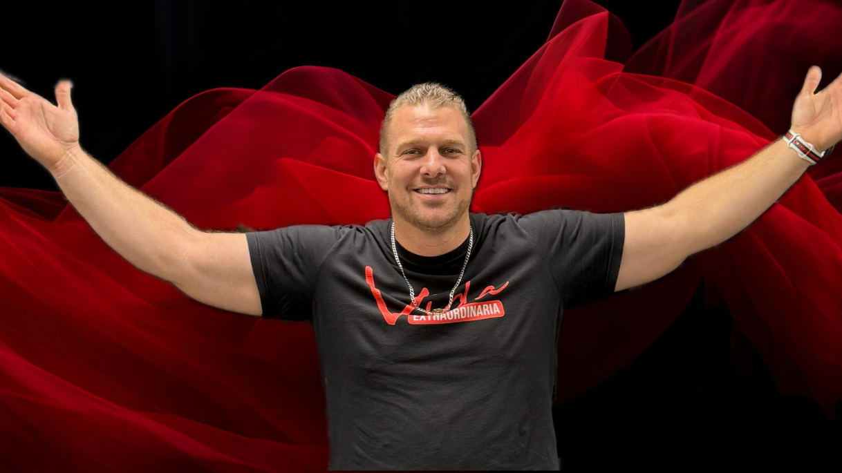 Hombre sonriendo con los brazos abiertos frente a una tela roja en movimiento.