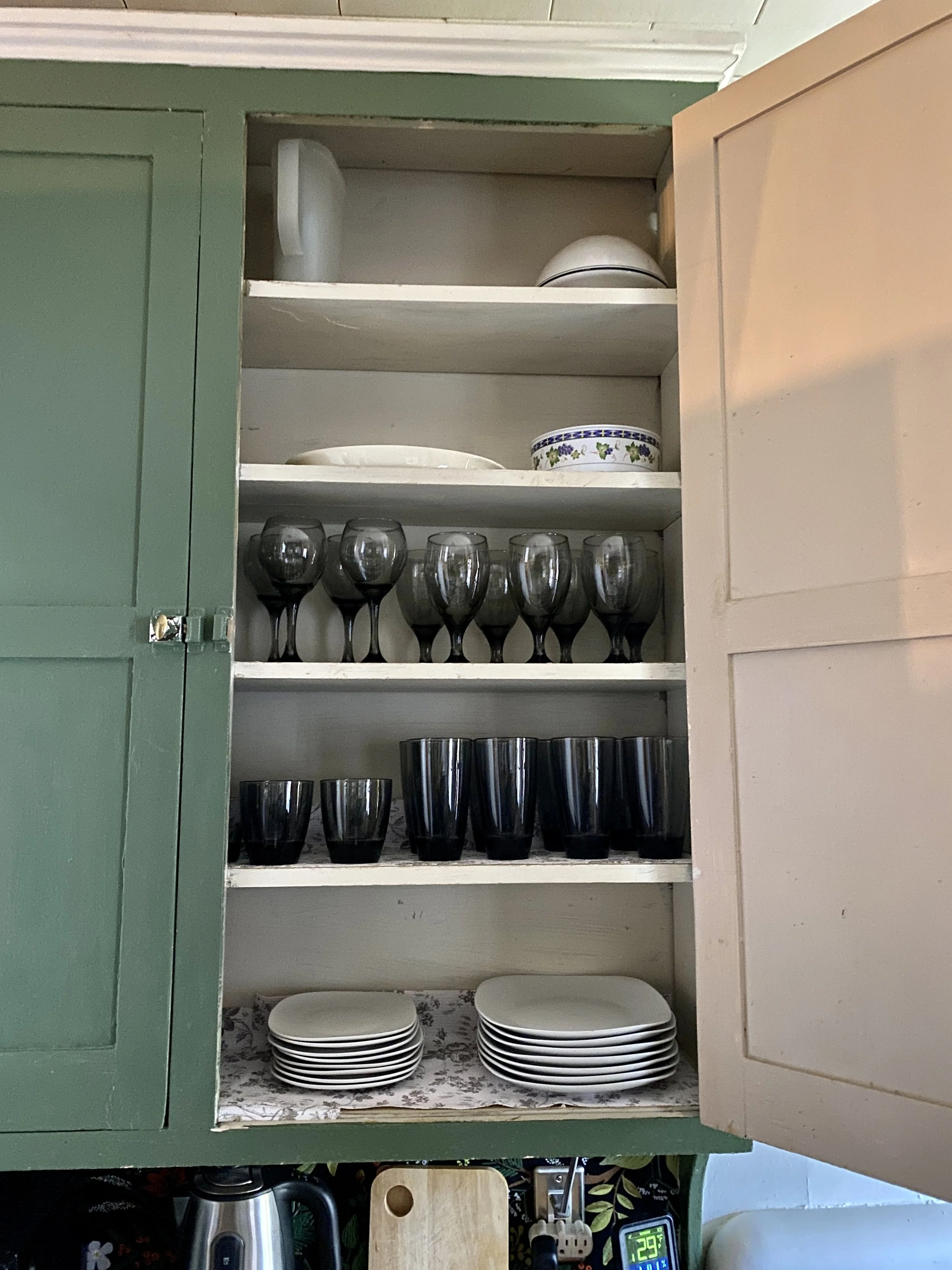 Kitchen cabinet with shelves holding plates, glasses, and bowls, with a green exterior and open door.