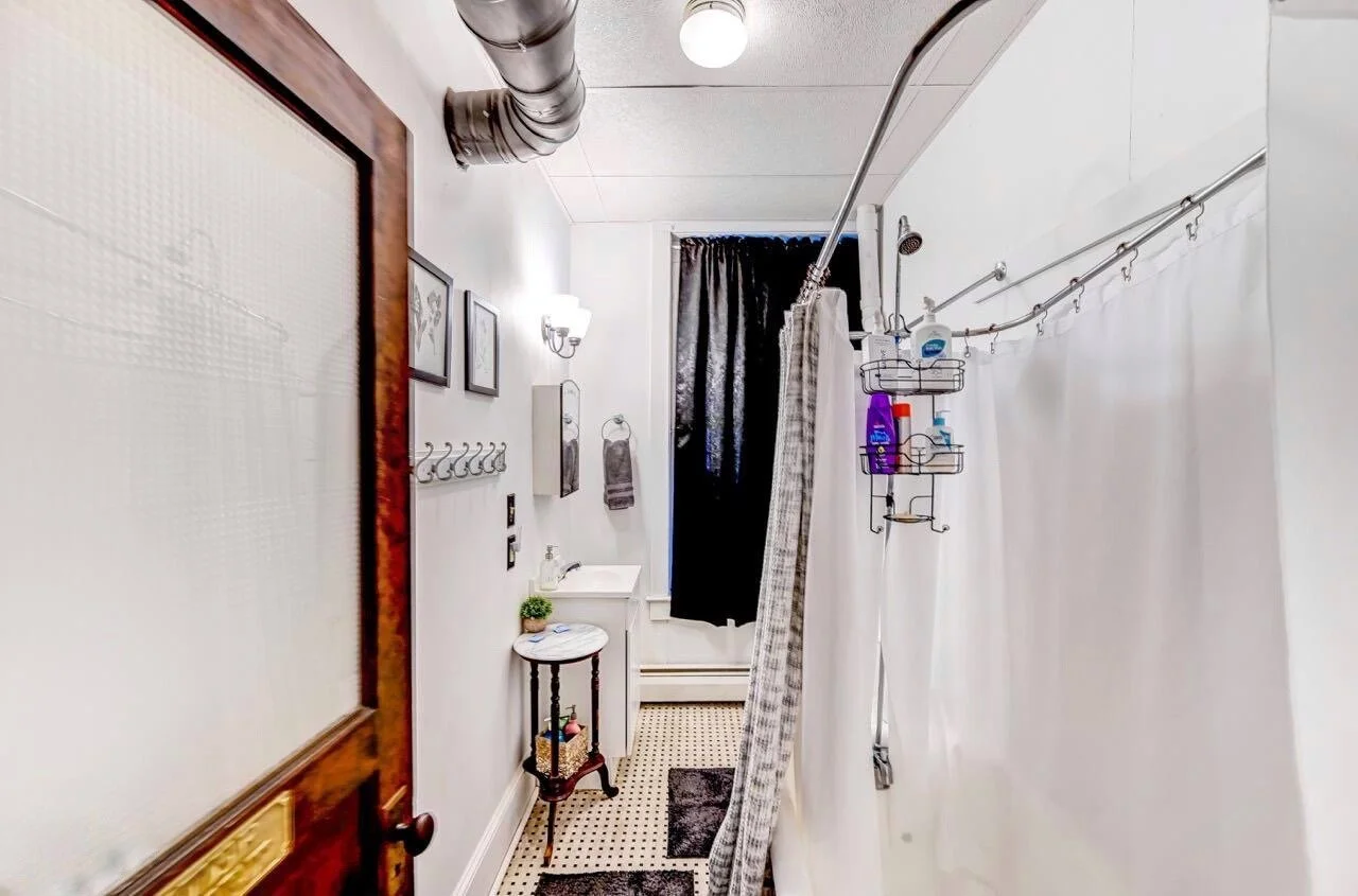 Small bathroom with a shower curtain, black and white checkered flooring, and various wall decorations.