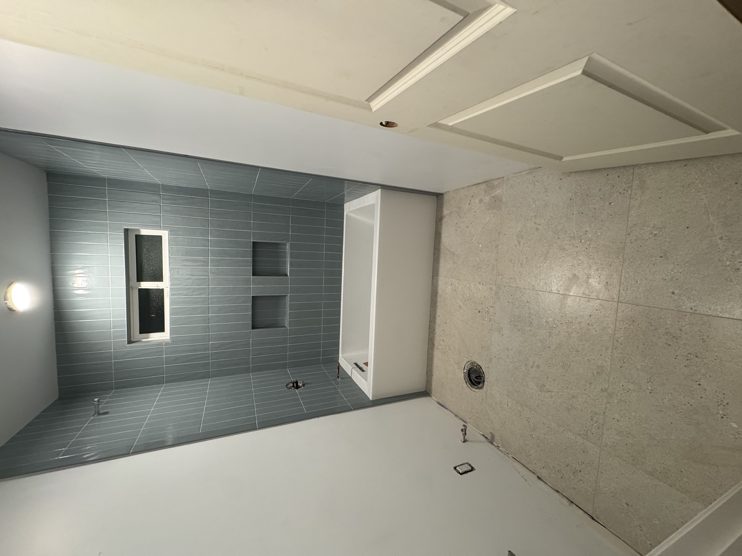 Bathroom under construction with gray tiled accent wall, bathtub, and unfinished flooring.