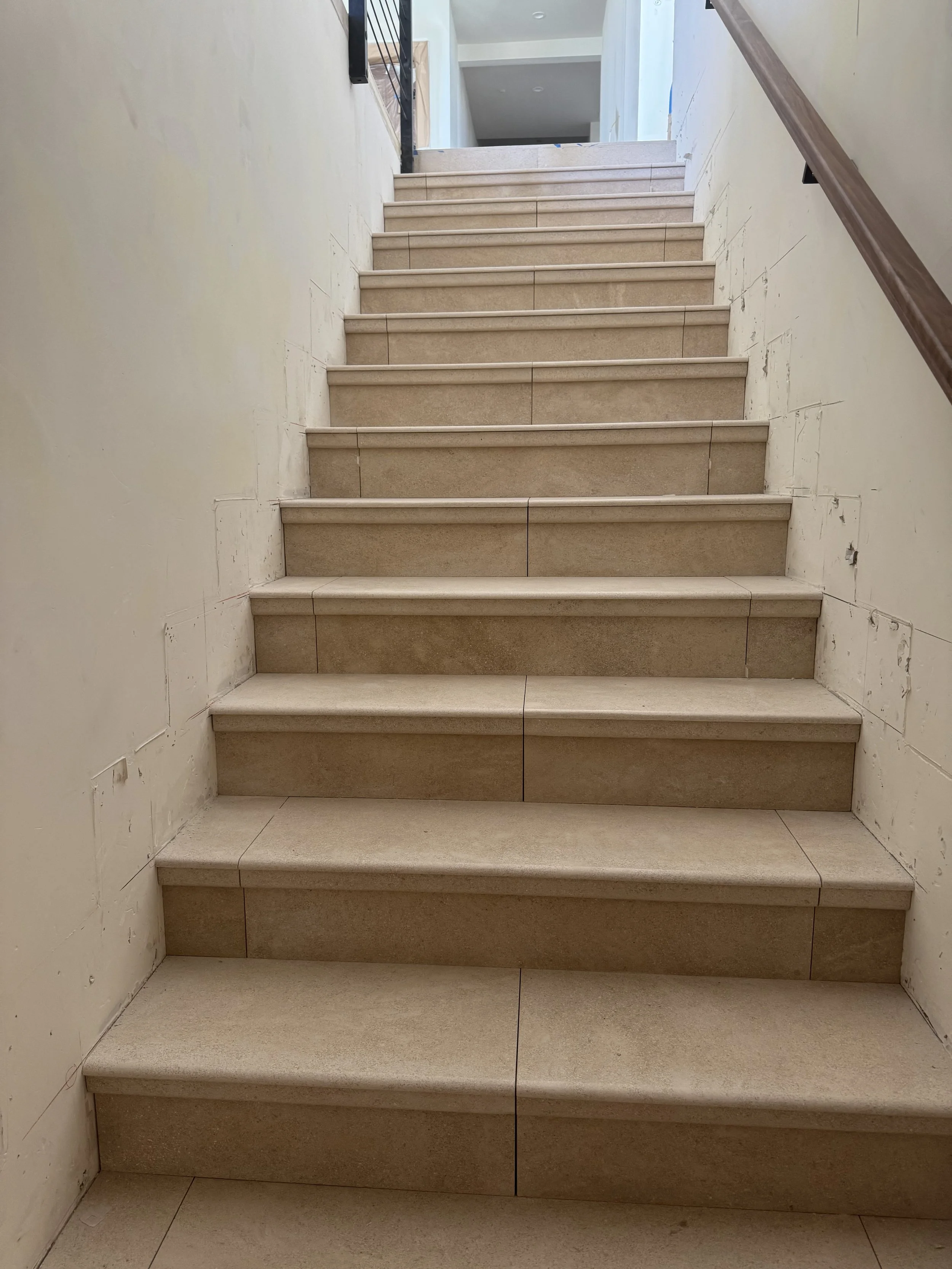 Indoor staircase with beige tiles and a wooden handrail on the right side.
