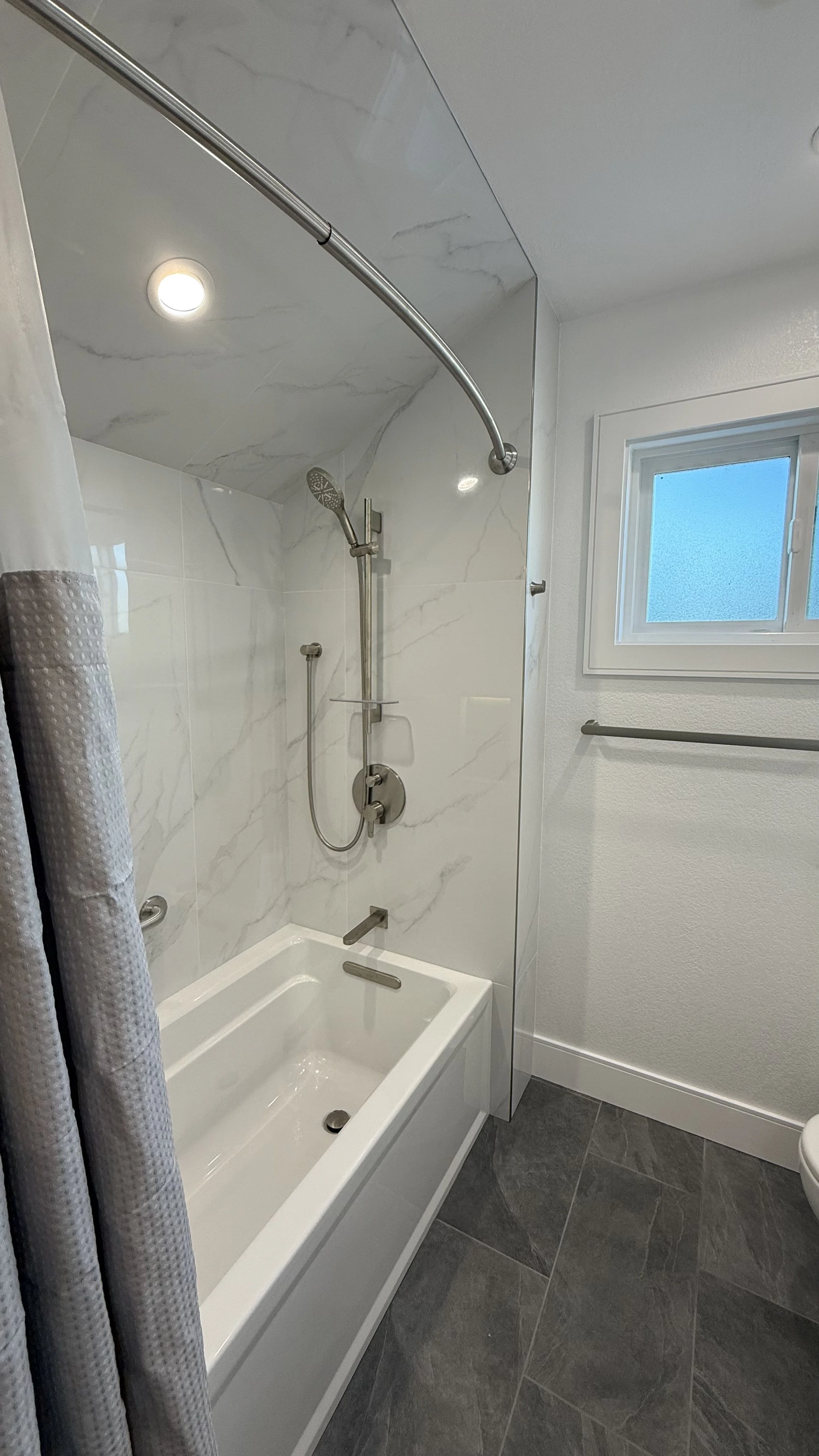 Bathroom with a bathtub, showerhead, white marble-like tile on the wall, a window, and a towel bar