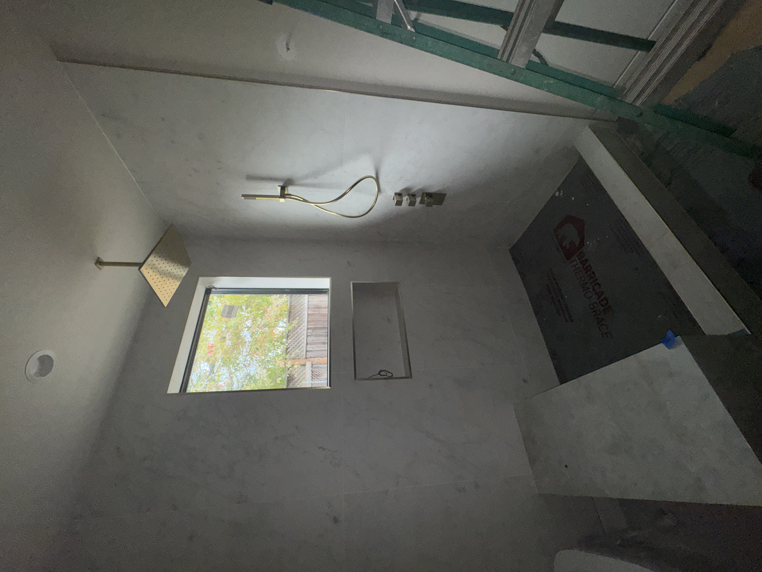 Unfinished kitchen with a window, a ceiling light fixture, an exposed electrical wire, and cabinetry installation in progress.