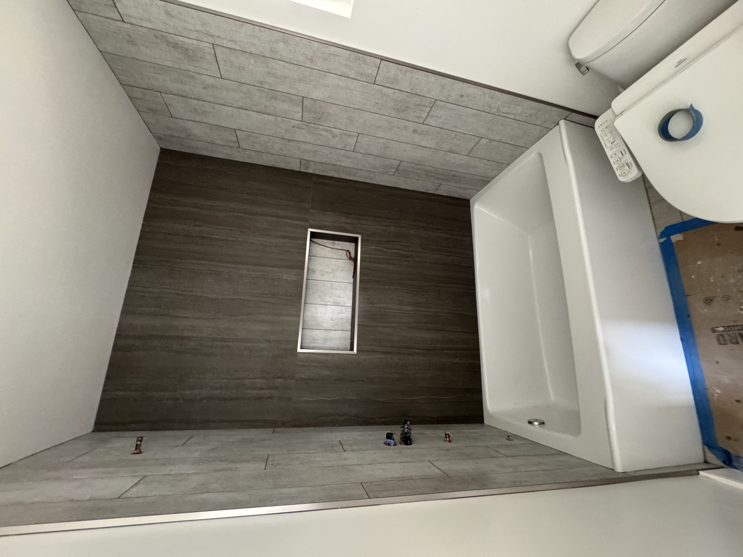  bathroom with gray tile walls and wood-look tile floor, a white bathtub