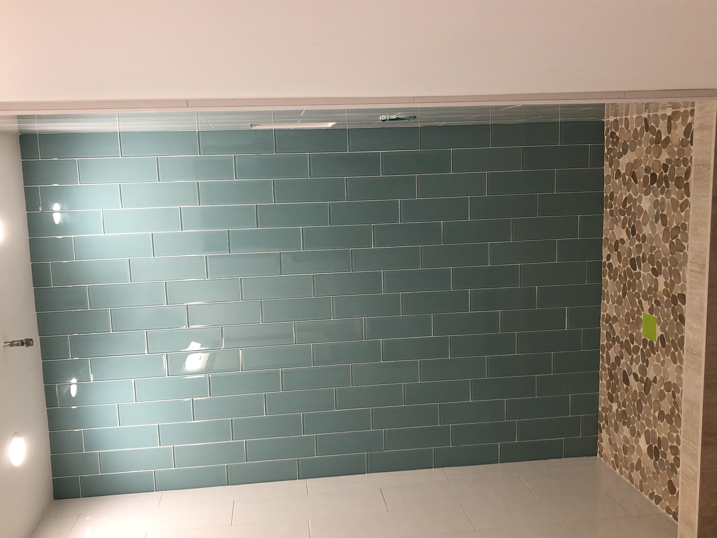 Interior of a modern bathroom with a green tiled wall, pebble stone floor, and ceiling lights.
