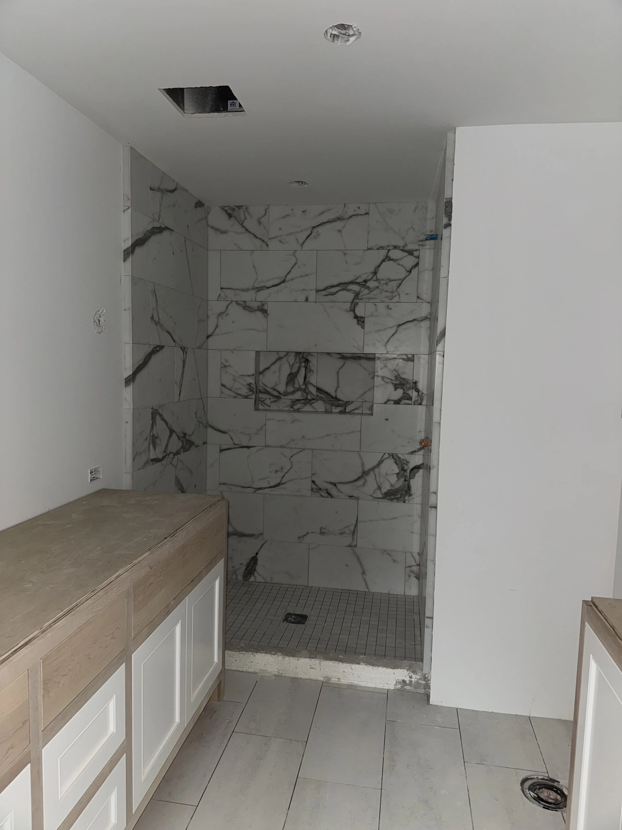 Bathroom shower area under construction with marble tiles and partial cabinet installation.