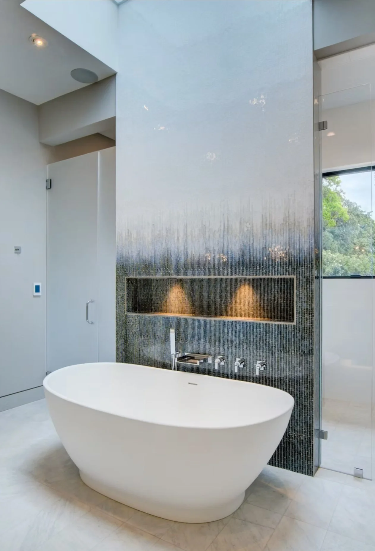 Modern bathroom with a freestanding white bathtub, mosaic tile wall, and glass shower enclosure.