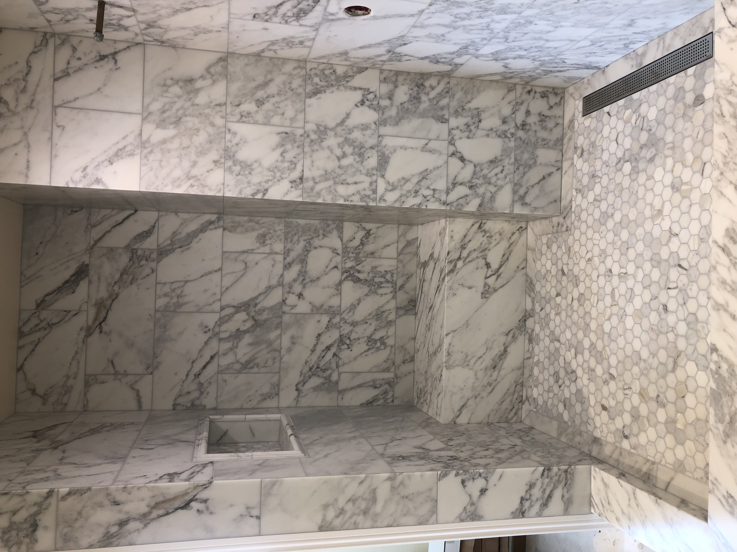 Marble shower with niches, tiles, and a drain on the floor.