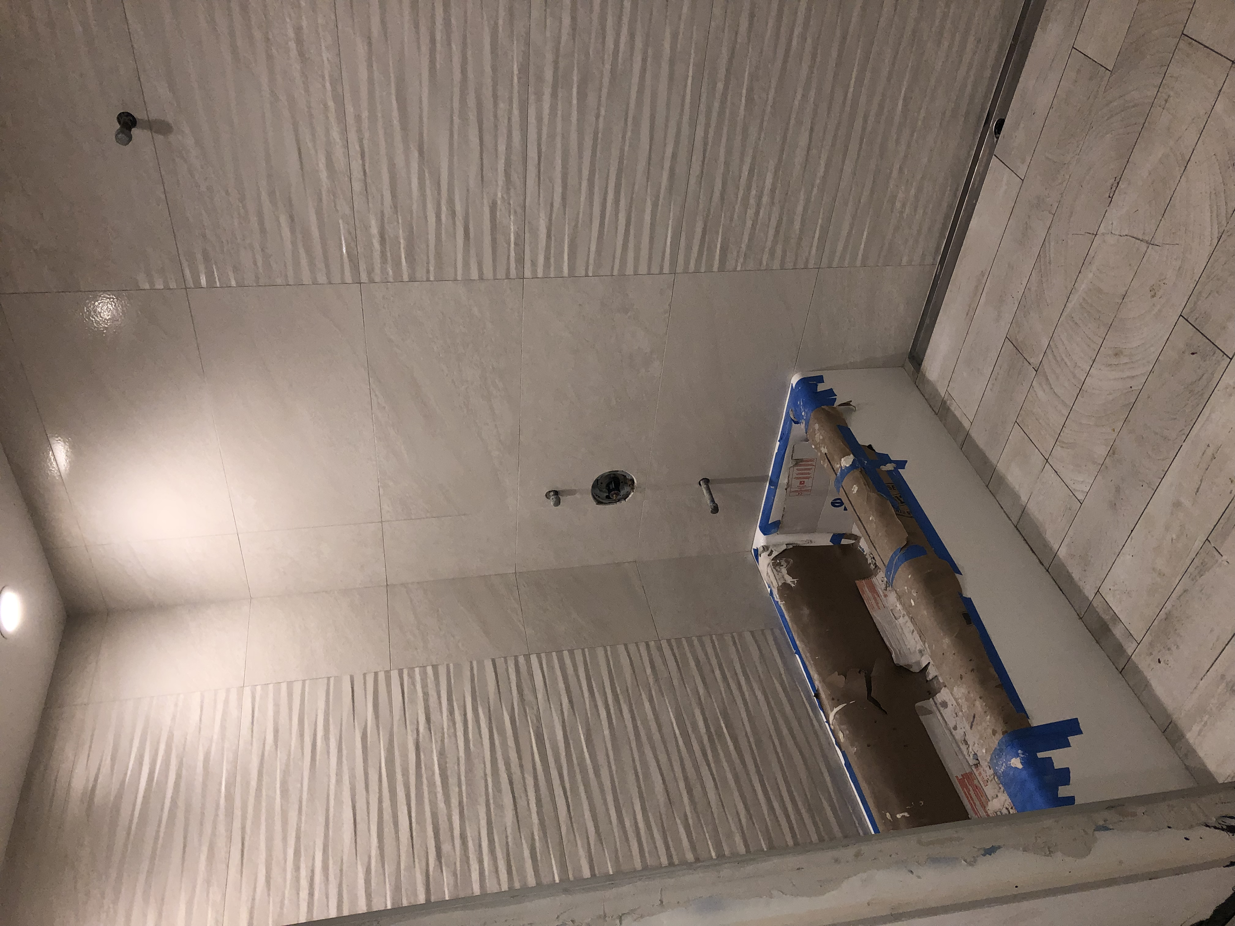 Bathroom wall and floor tiles under construction with pipes and a toolbox.