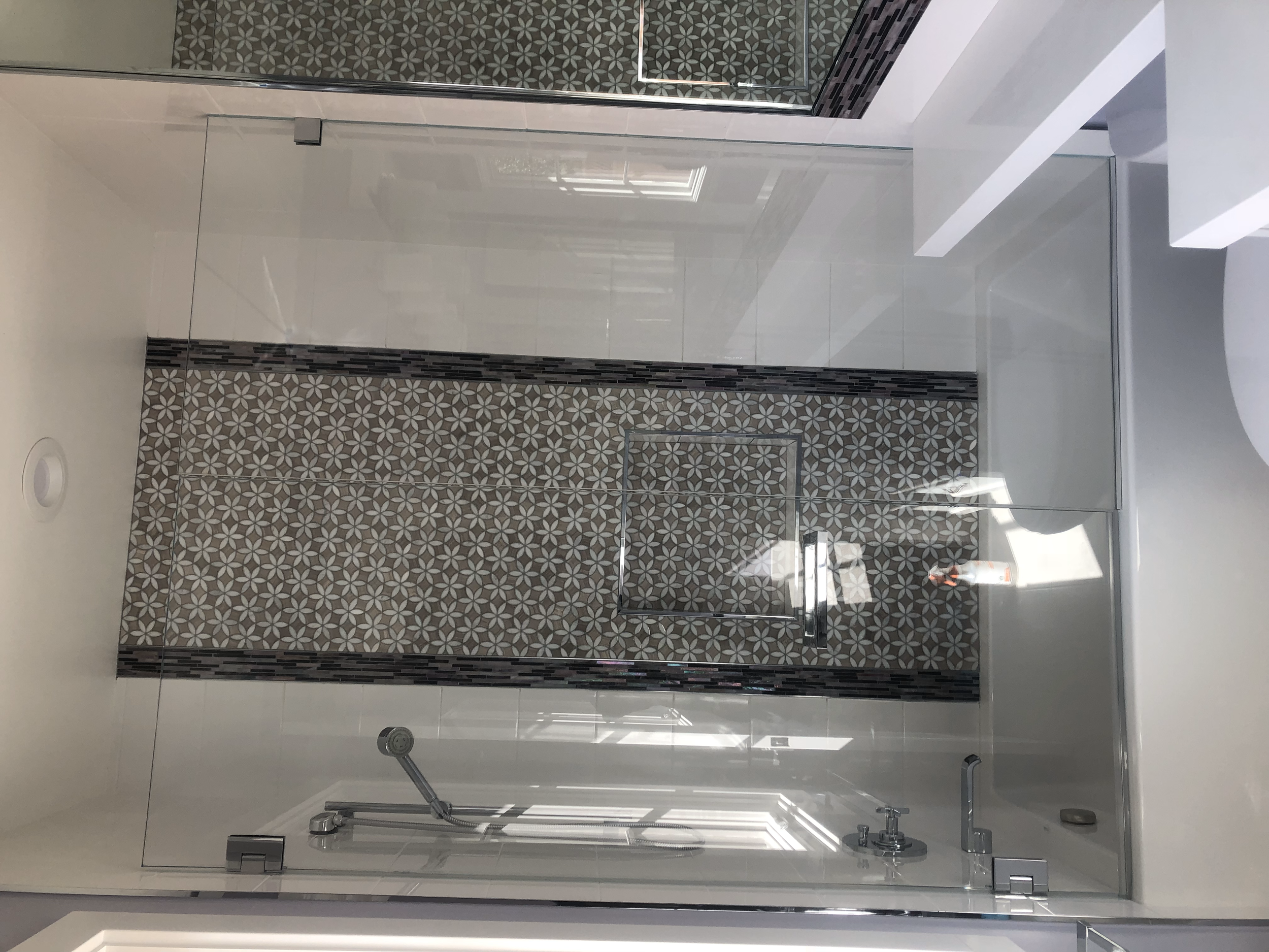 Modern bathroom with glass shower enclosure, geometric tile design in the shower, and minimalist fixtures.