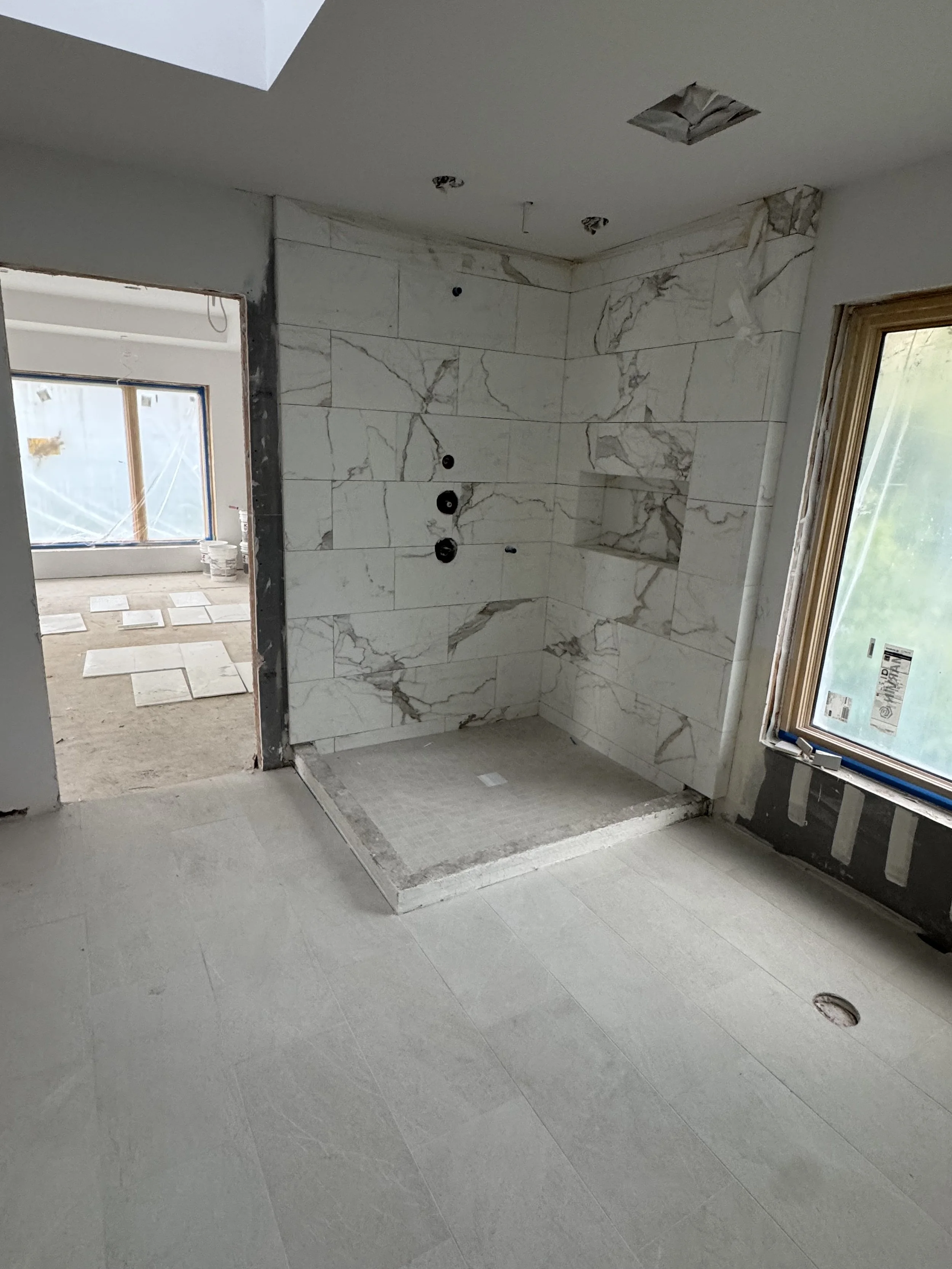 Bathroom under construction with a marble-tiled shower area, a window, and construction materials on the floor.