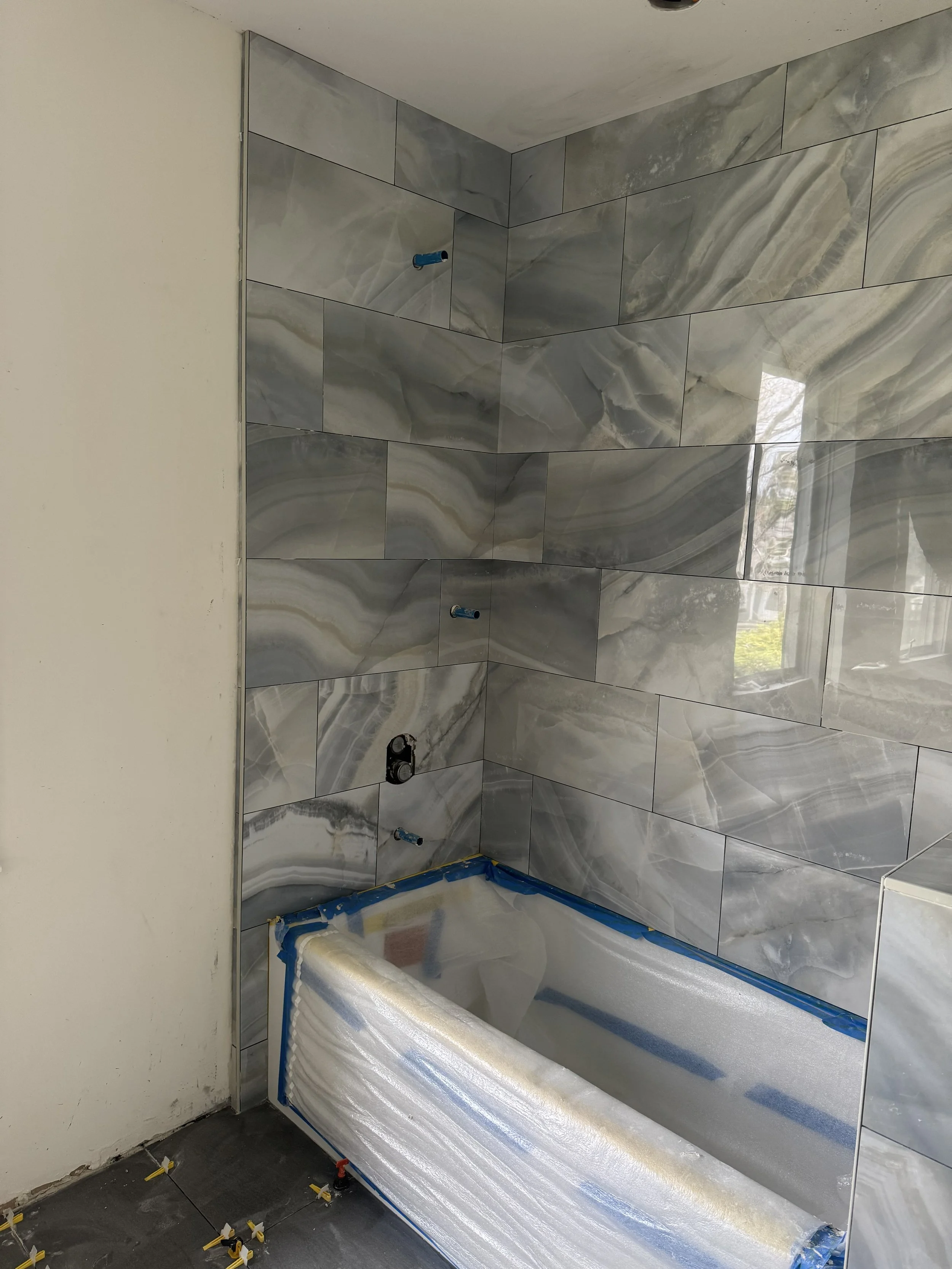 Bathroom under construction with gray marble wall tiles and an installed bathtub covered with protective foam and tape.