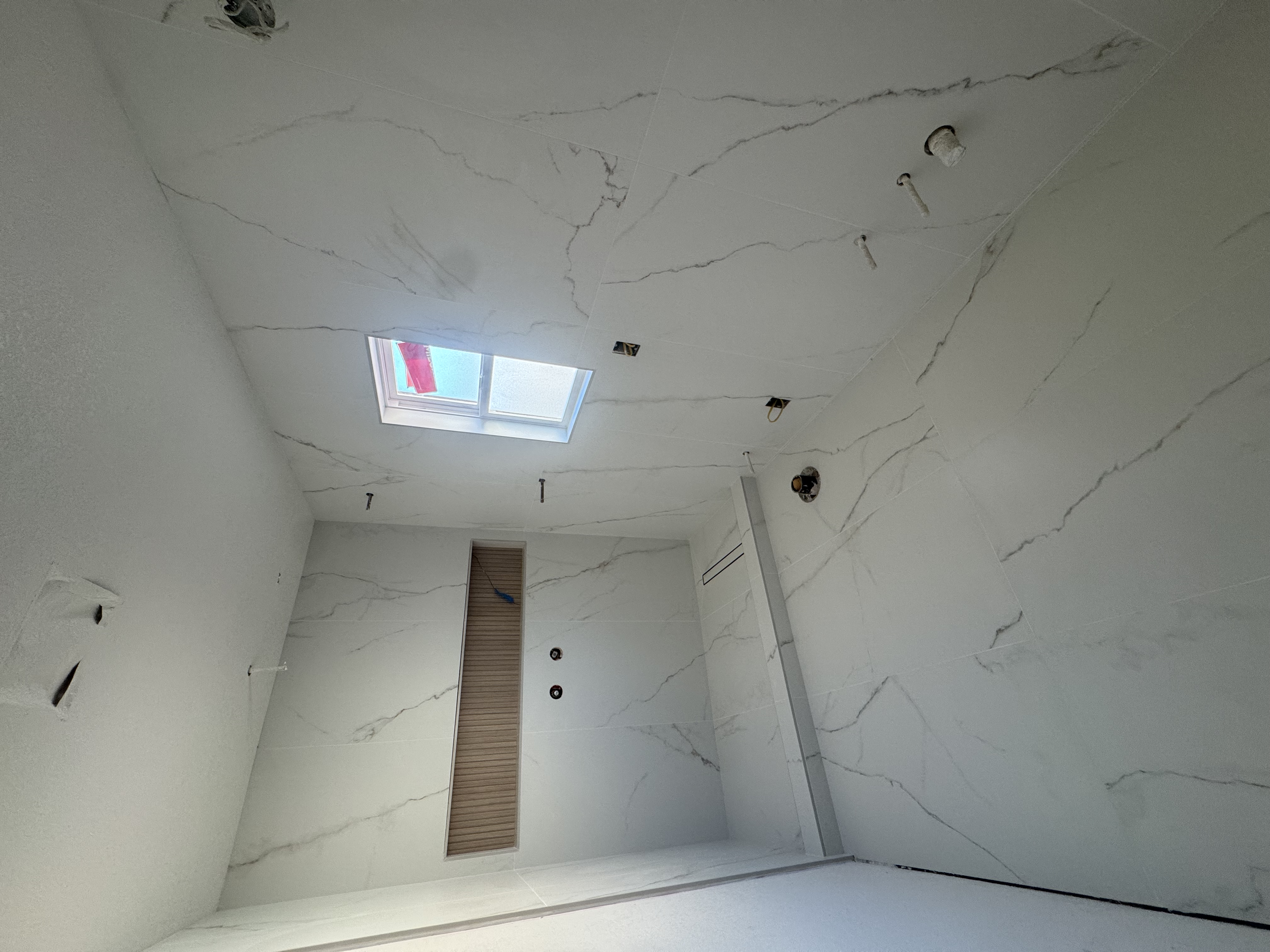 Bathroom under construction with marble walls, a skylight, and fixtures not yet installed.