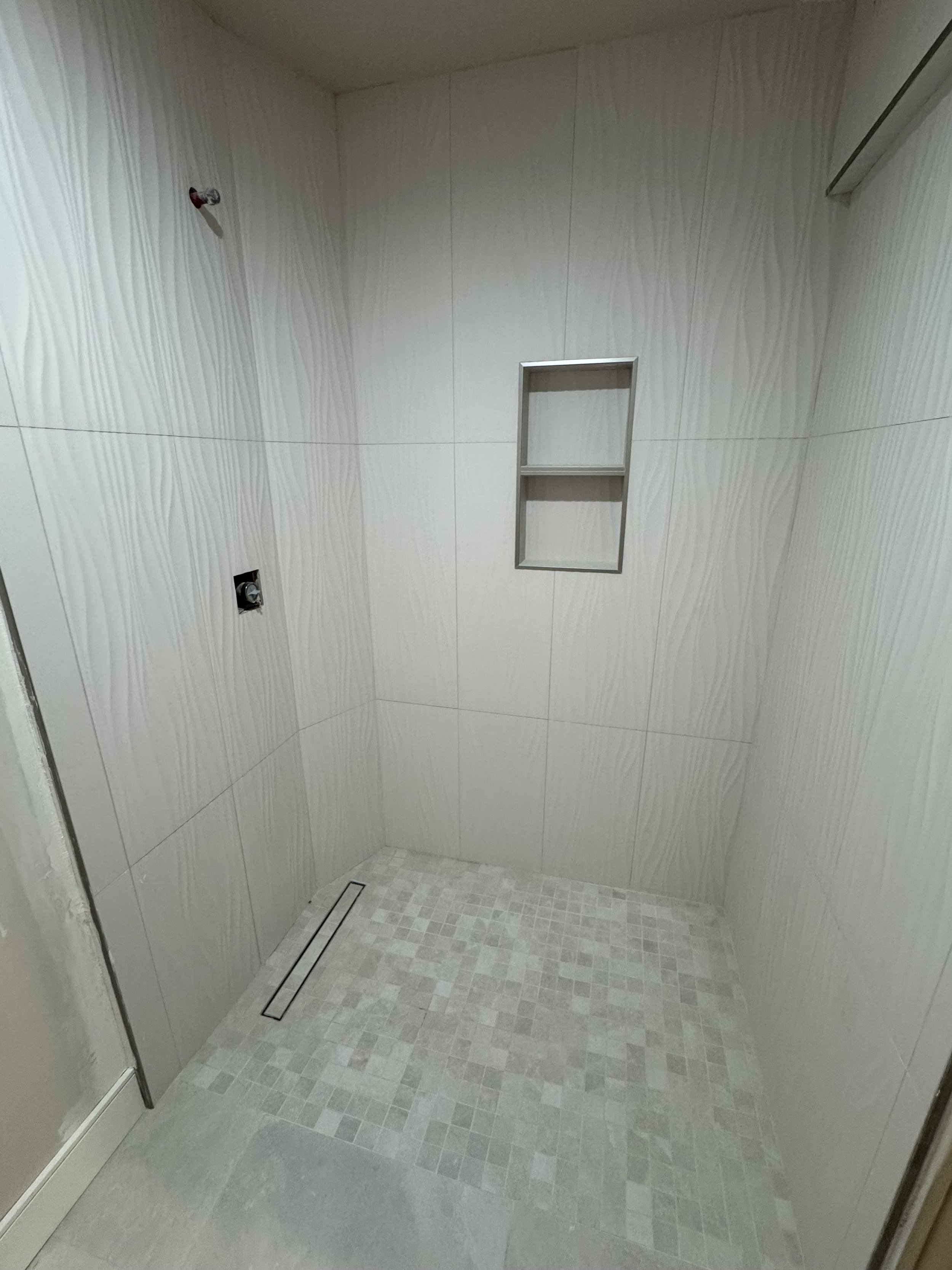 Empty shower with tiled walls, a built-in shelf, and a drainage grate on the floor.