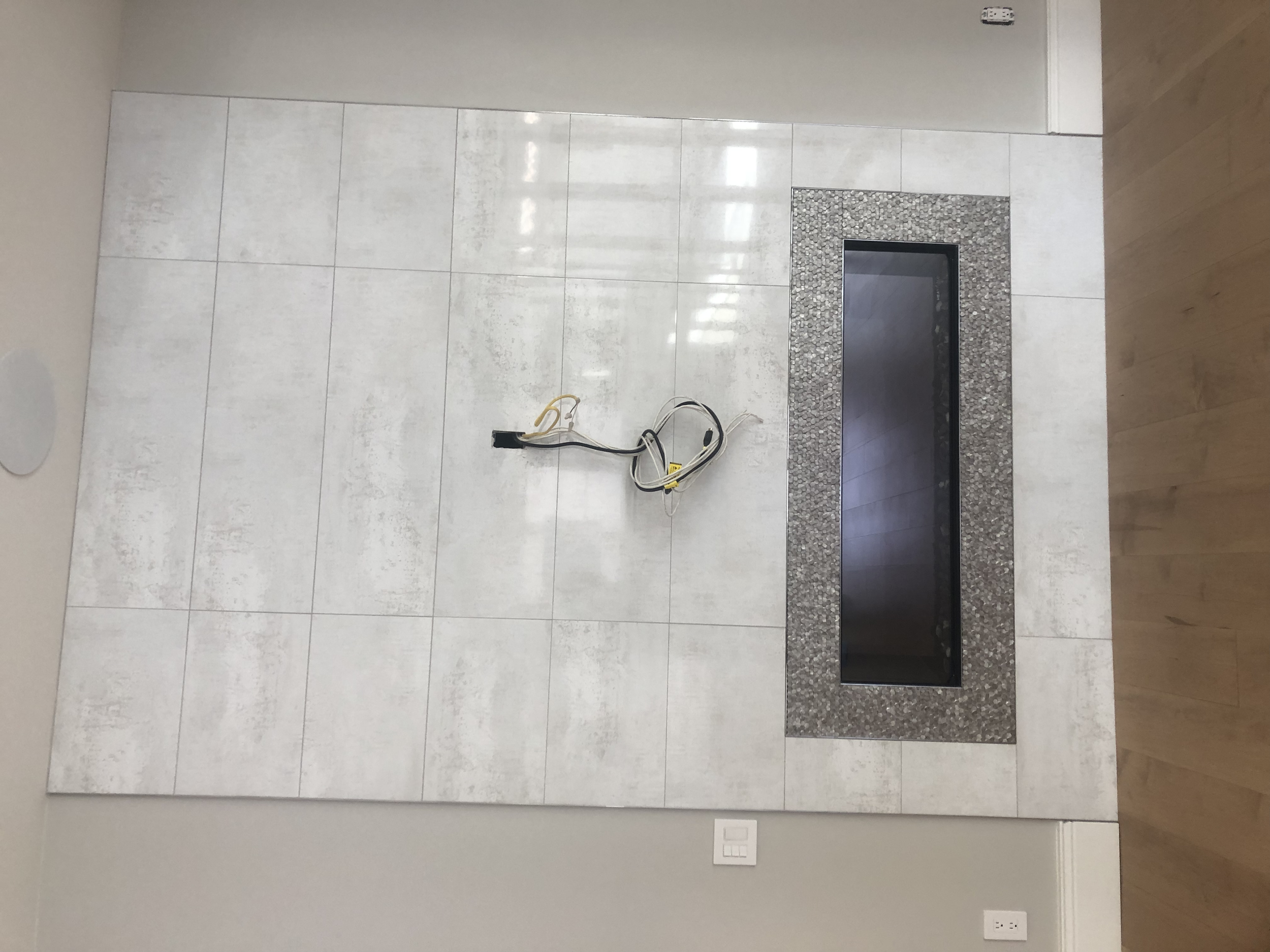 Empty fireplace with a tiled surround and an electrical outlet on the wall.