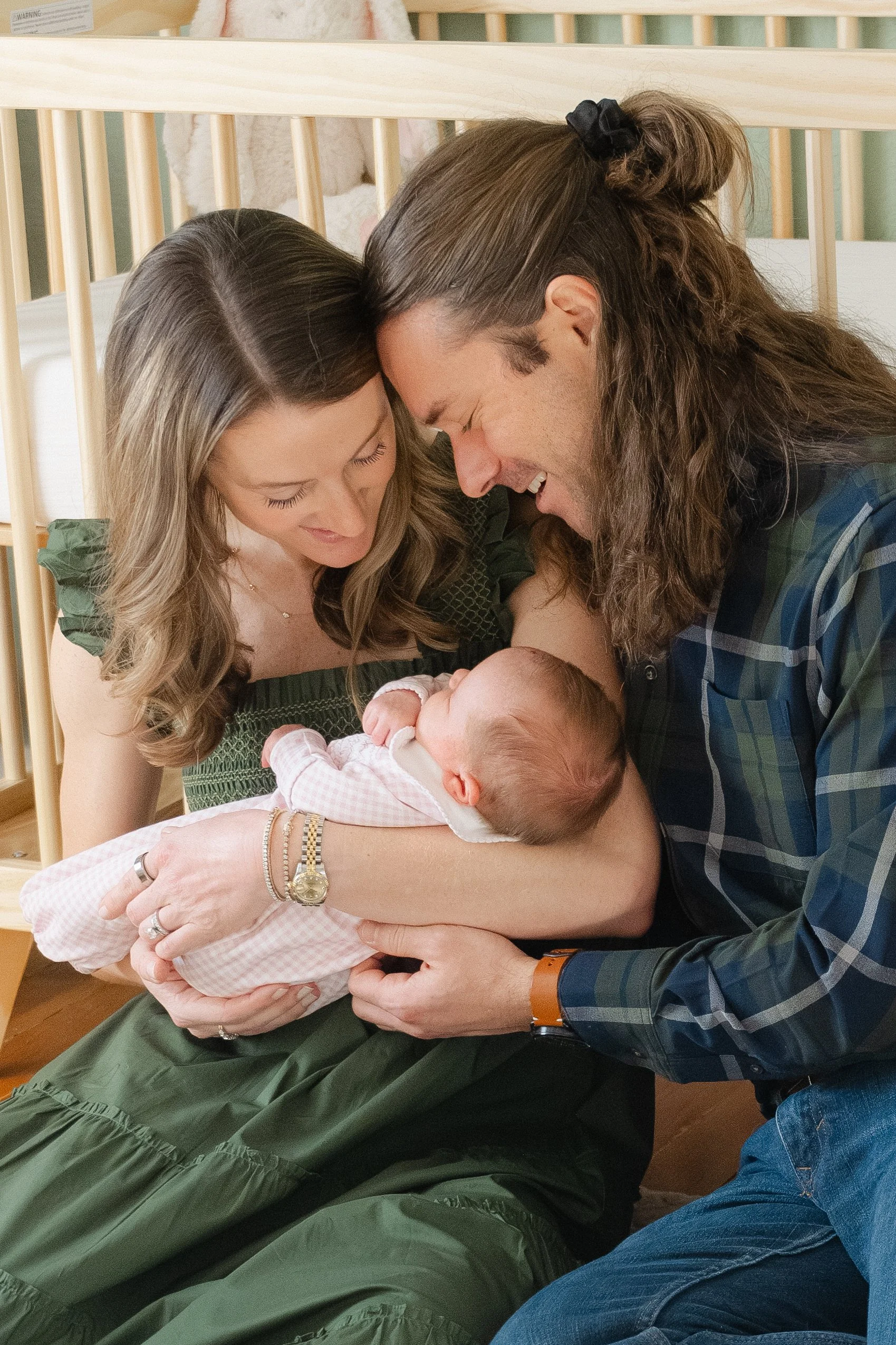 A woman and man holding and smiling at a newborn baby in a nursery.