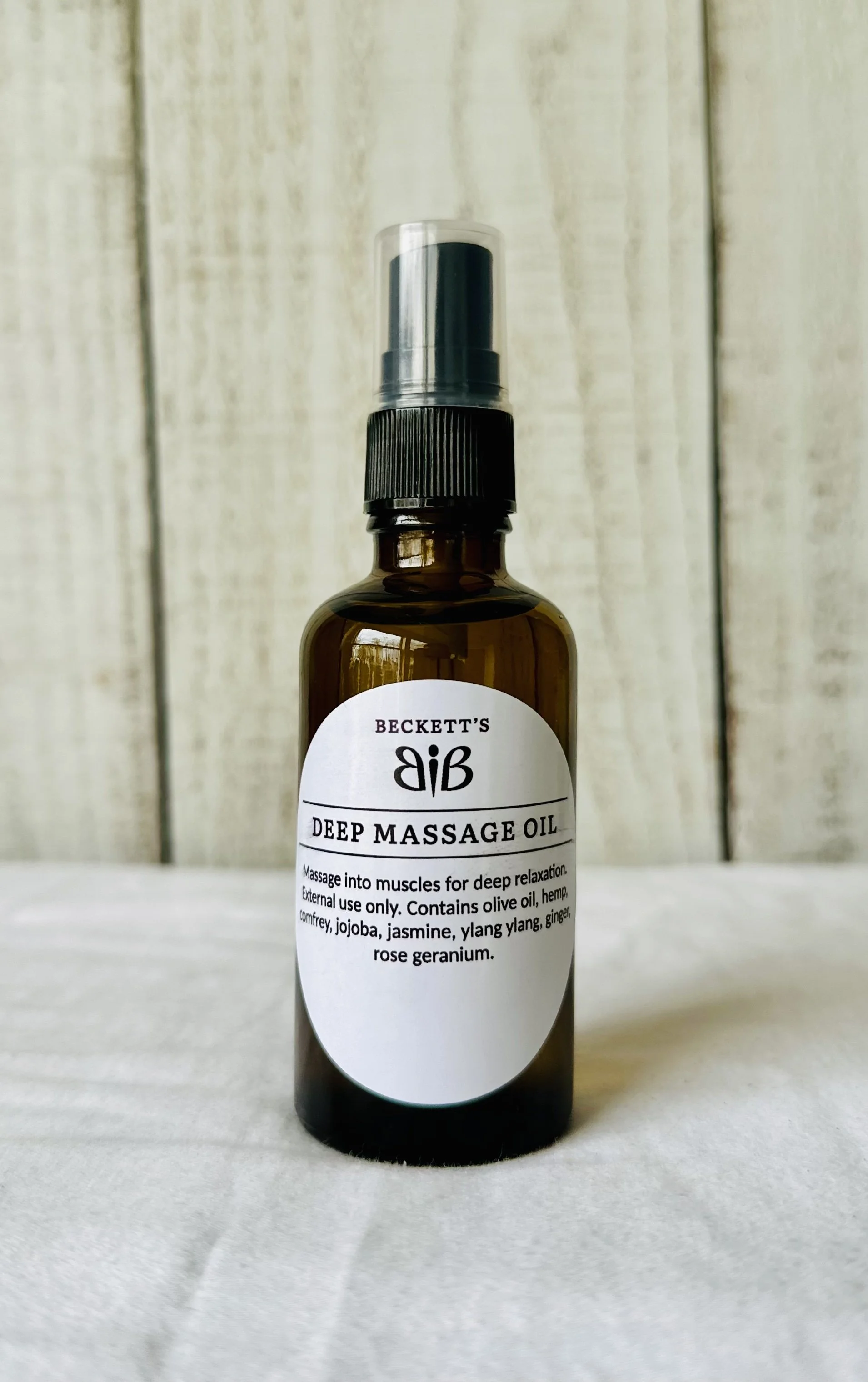 Amber glass bottle with a spray top labeled 'Beckett's Deep Massage Oil' on a white surface with a light wooden background.