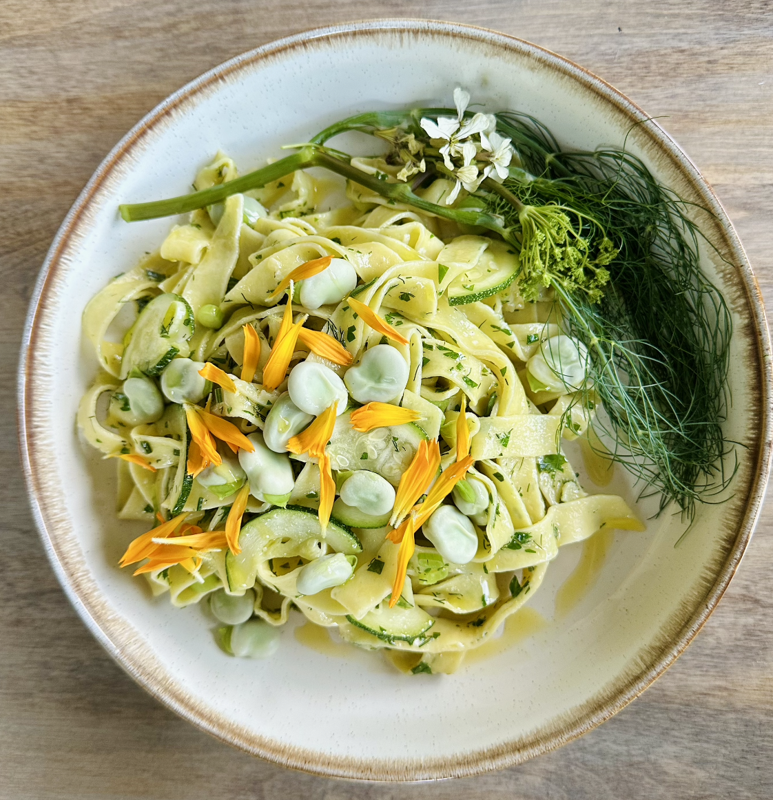 Bowl of pasta with green vegetables, topped with edible flowers and herbs.