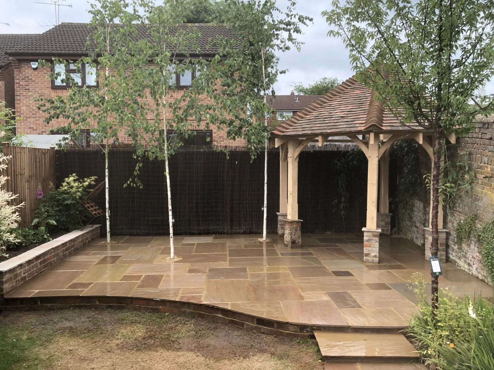 A backyard with stone patio, a oak framed gazebo