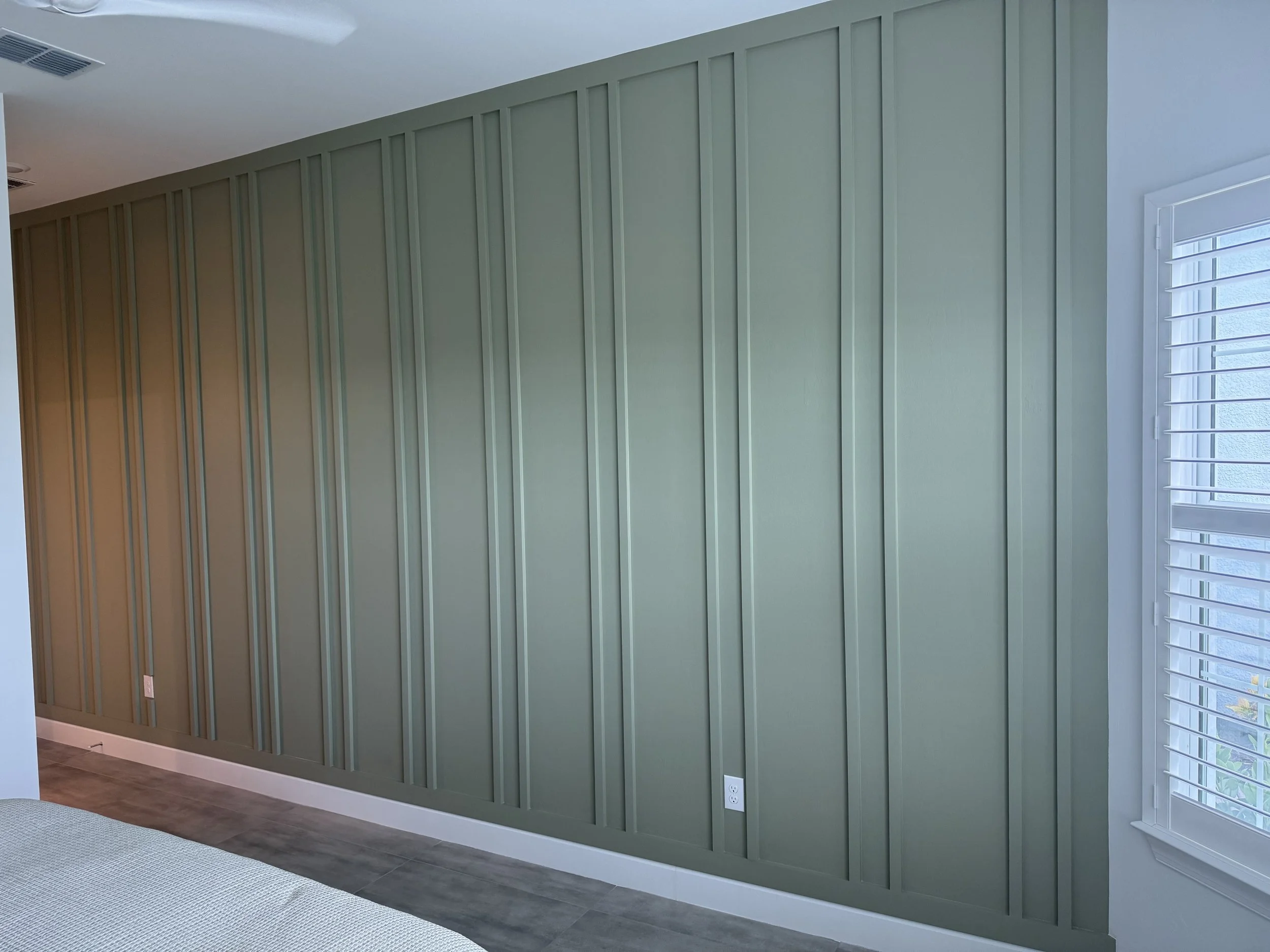 Green paneled accent wall in a bedroom with a window and a partial view of a bed. Wood accent wall, Accent Painting, Venice Florida, Venice Paint & Carpentry