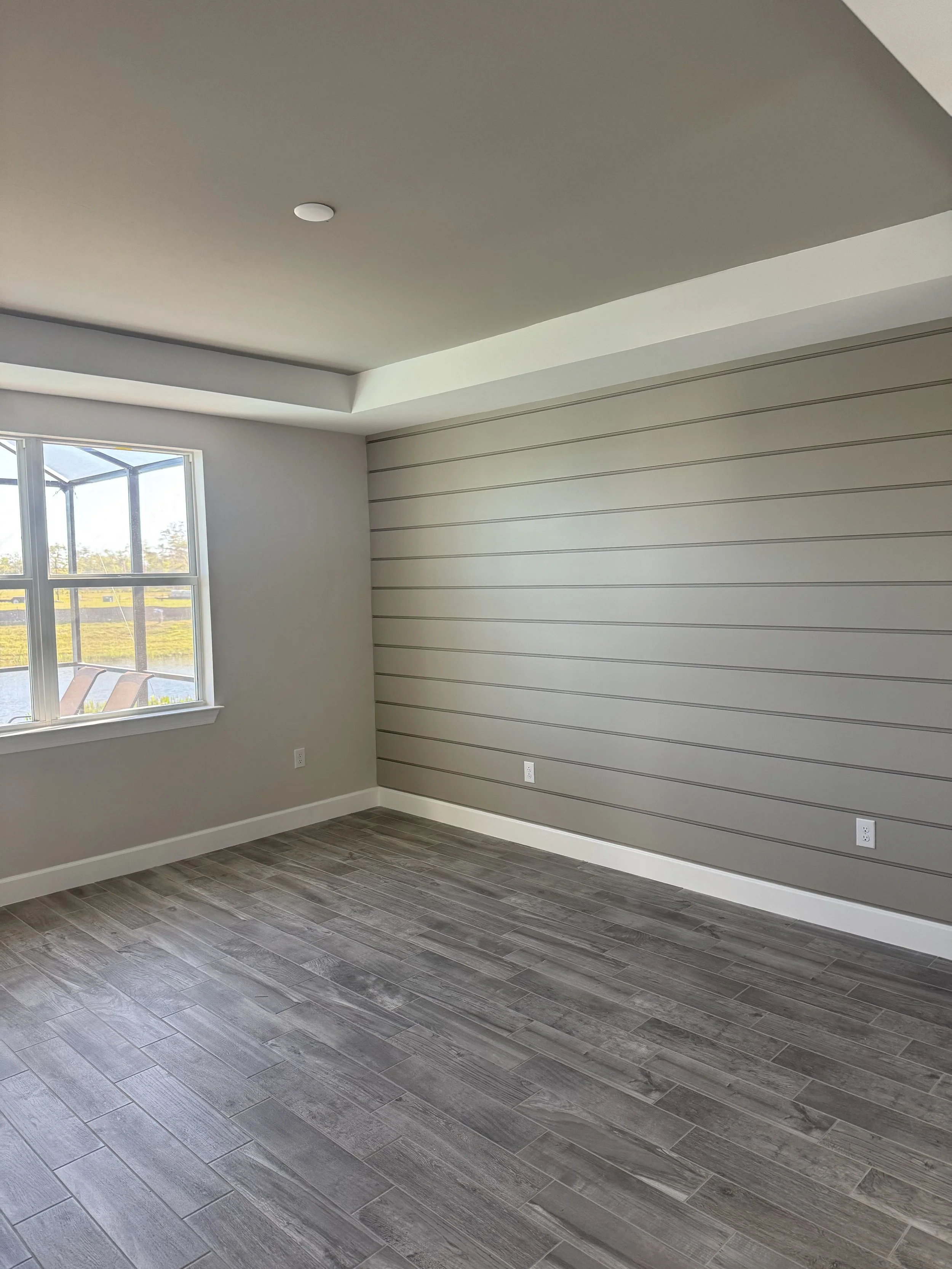 Empty room with a window, wood-look tile flooring, a gray wall with horizontal lines, and a ceiling with a drop detail.