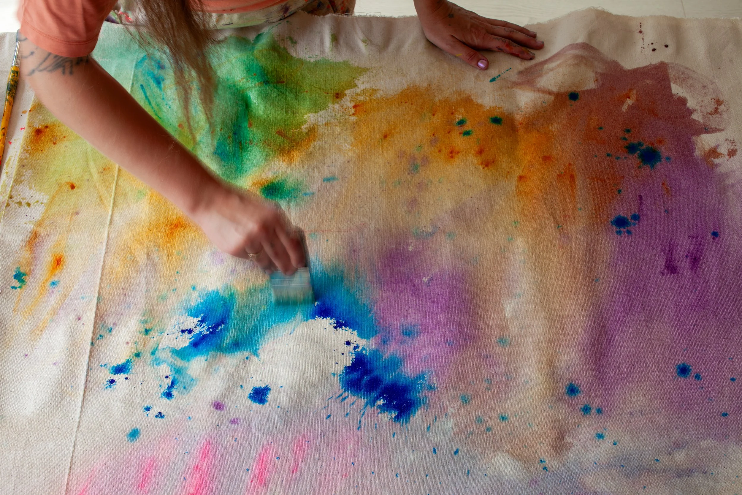 Person creating colorful abstract art on canvas using watercolor and brush.