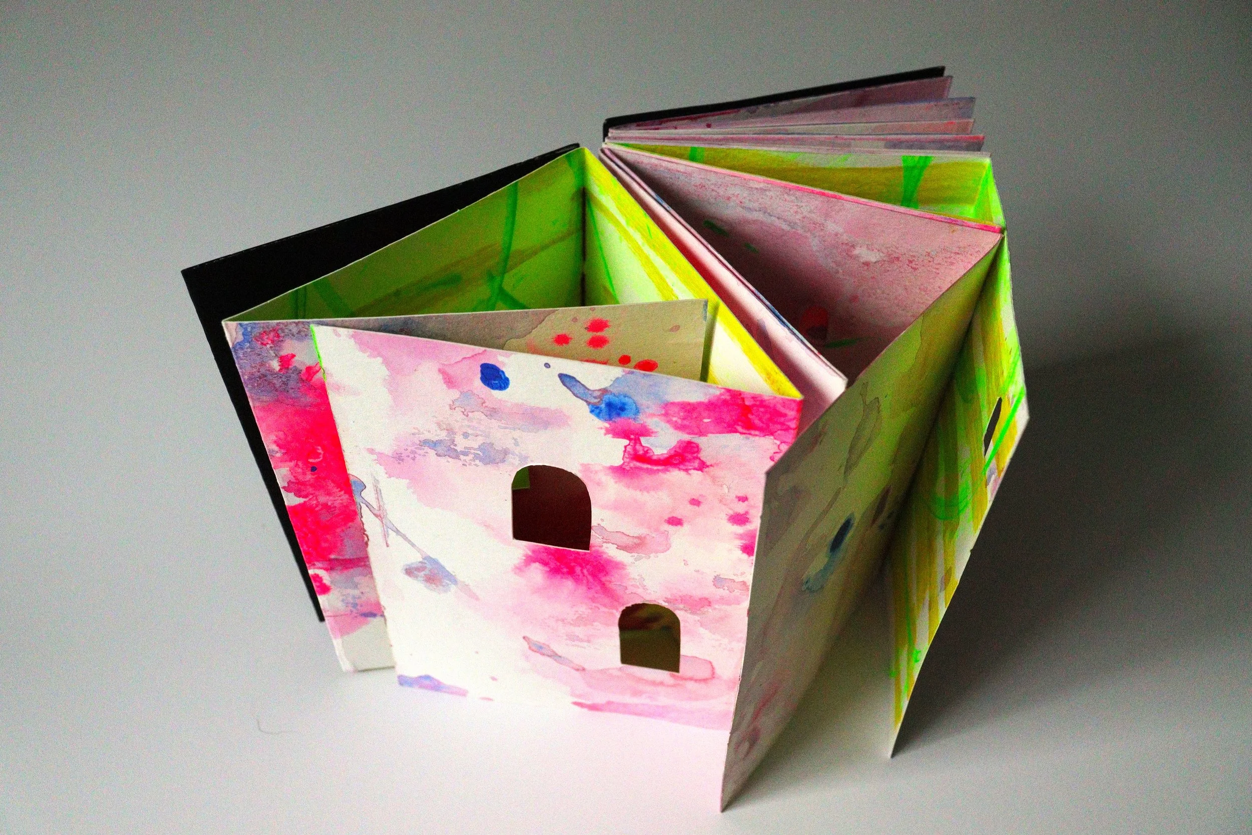 An open accordion-style paper folder with colorful abstract watercolor designs inside on a plain gray surface.