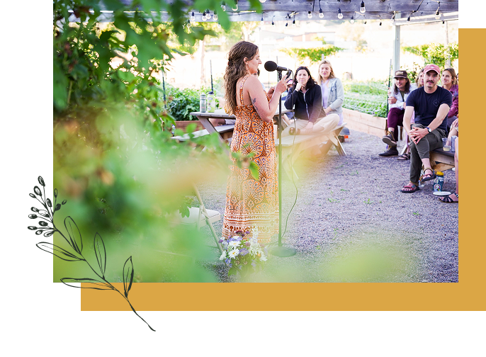 A woman in a patterned dress speaking into a microphone at an outdoor event with a small audience seated on benches. Millay and Meadowlark Flower Farm in Missoula, Montana. Weddings and Corporate events.