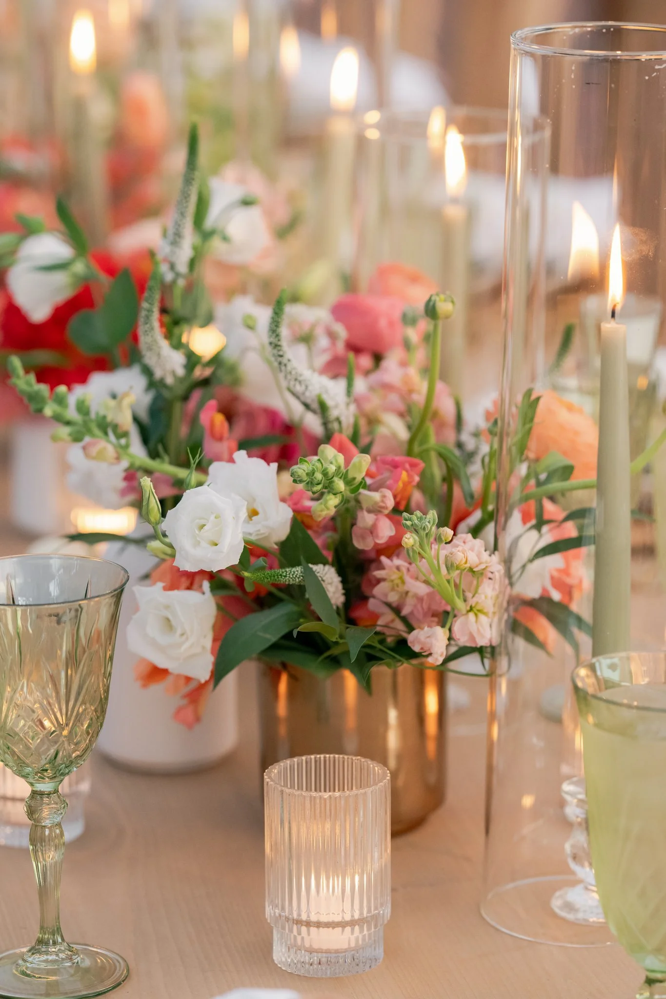A close-up of a decorated table with a floral centerpiece, candles in glass holders, and elegant glassware at an event or wedding reception.