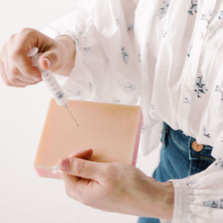 Person holding a syringe and a bar of soap or sponge