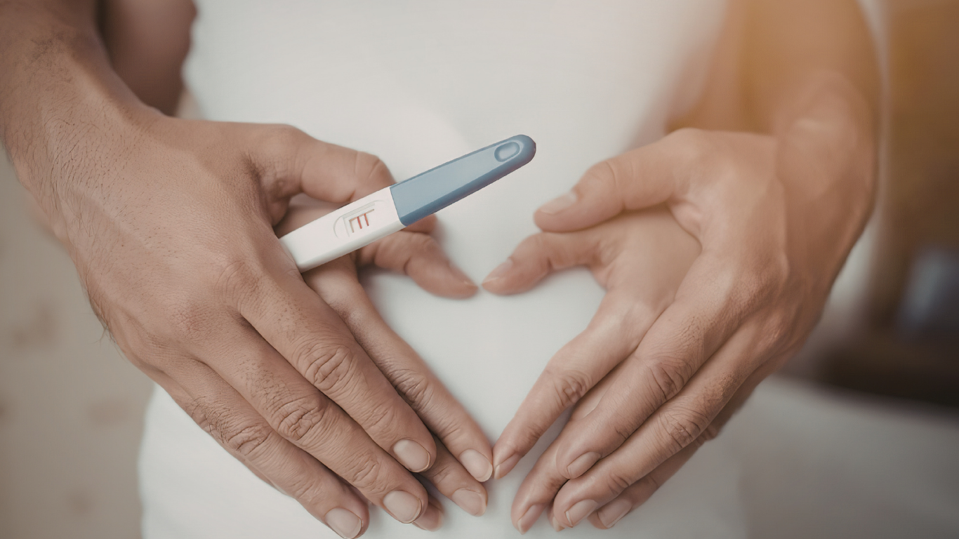 Hands forming a heart shape with a pregnancy test held in the middle.