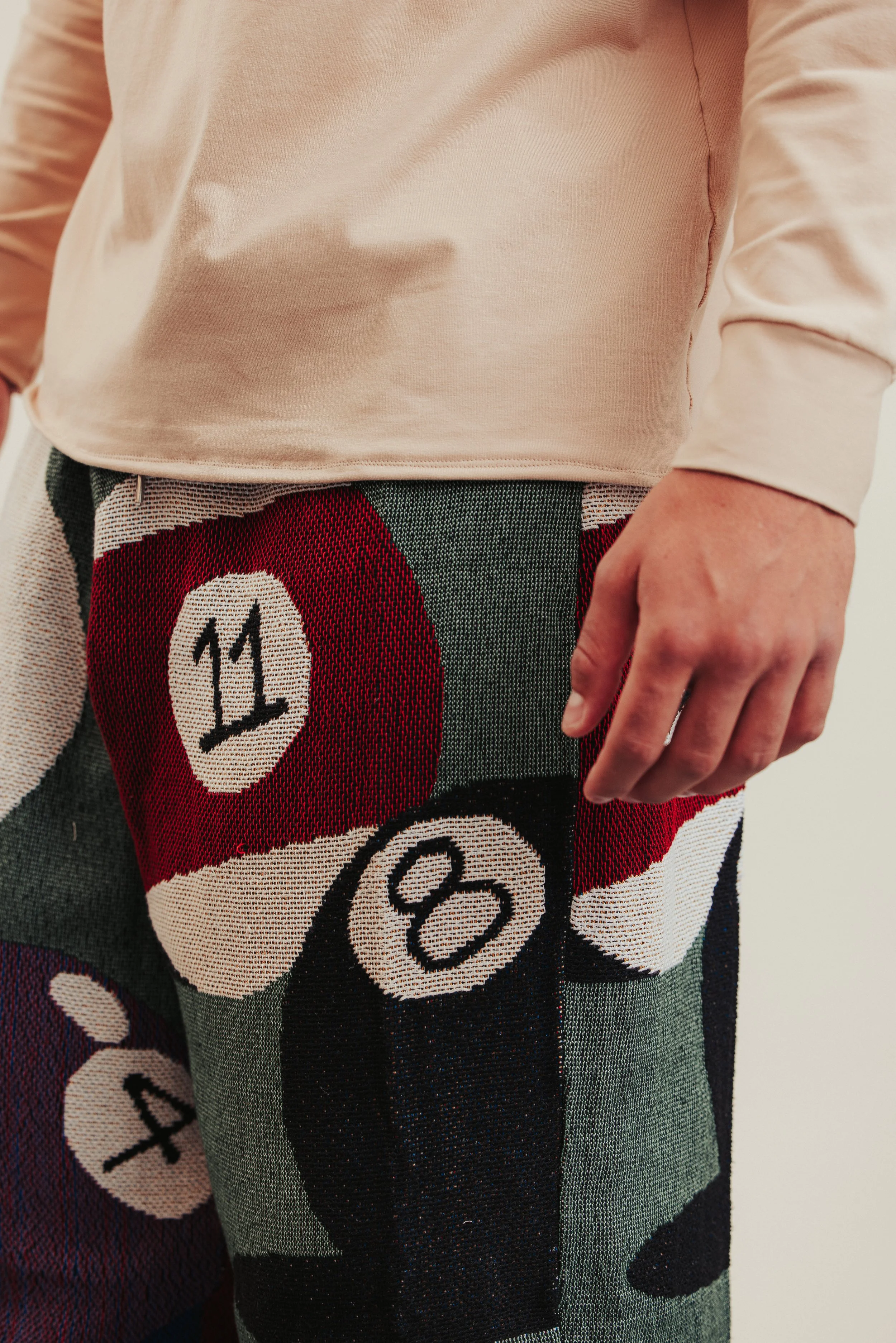 Close-up of a person's waist showing a beige shirt and colorful pants with bingo numbers pattern.