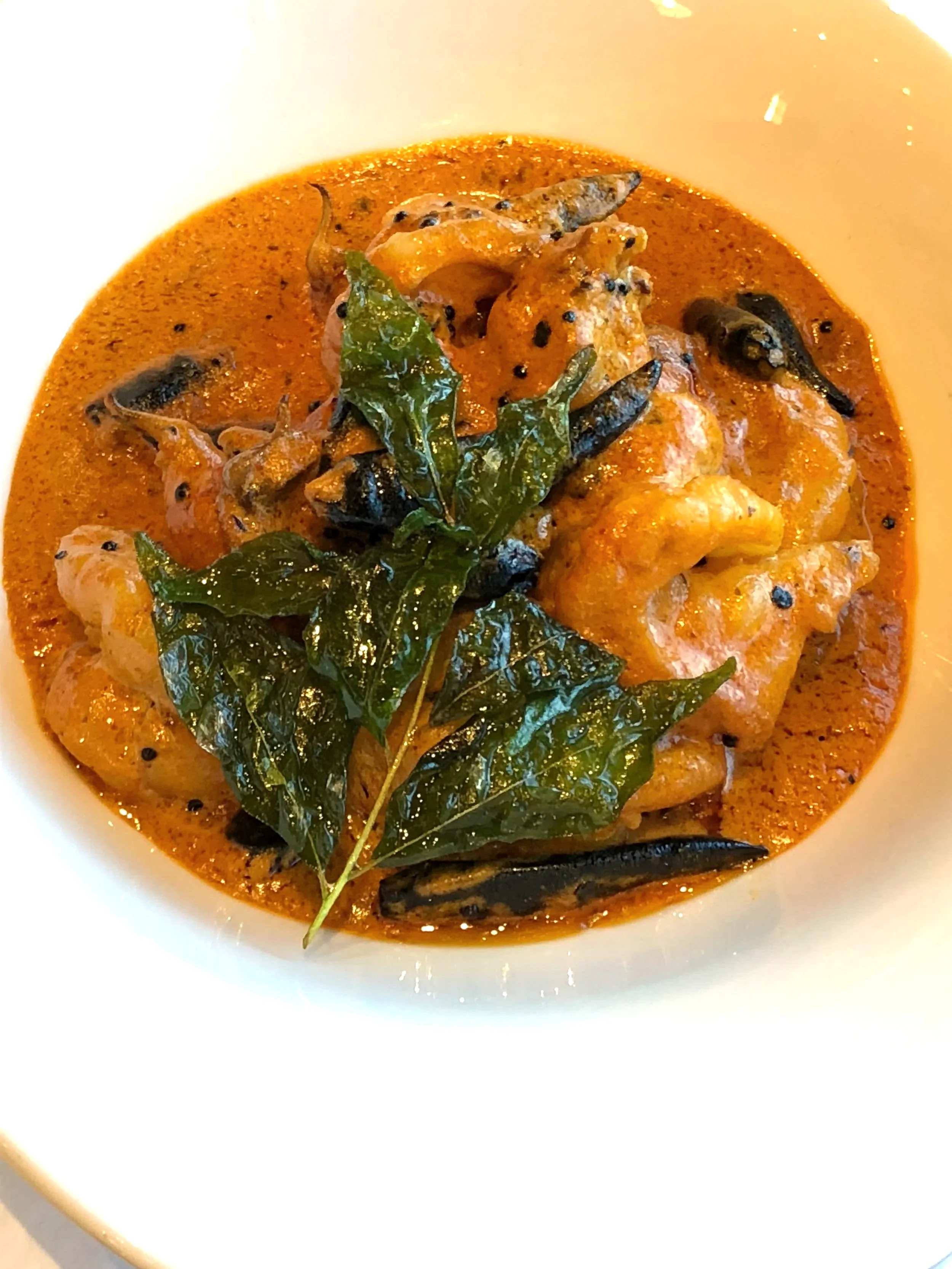 A bowl of spicy shrimp curry garnished with fresh green basil leaves.