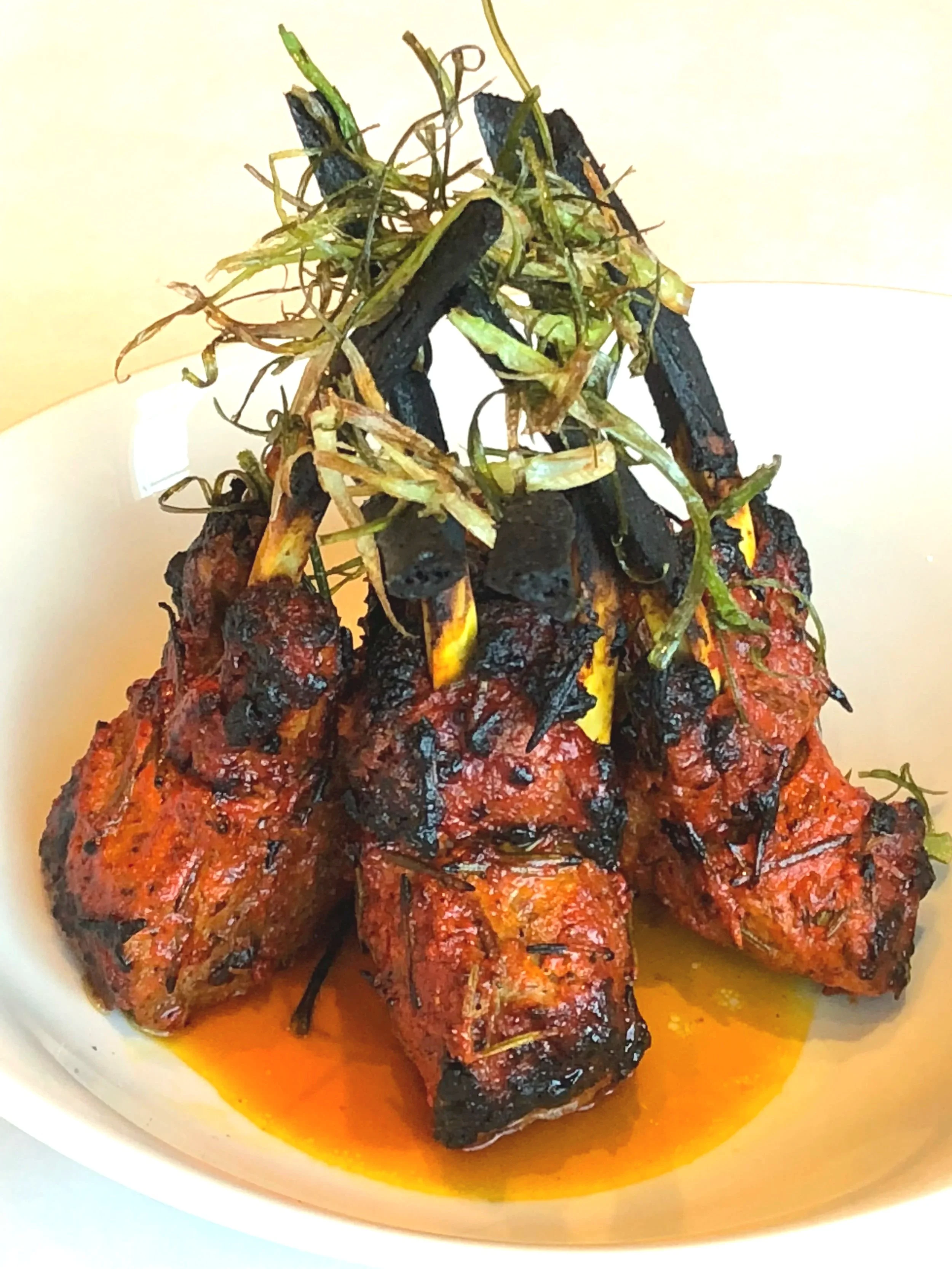 Grilled ribs with herbs and green onions on a white plate.