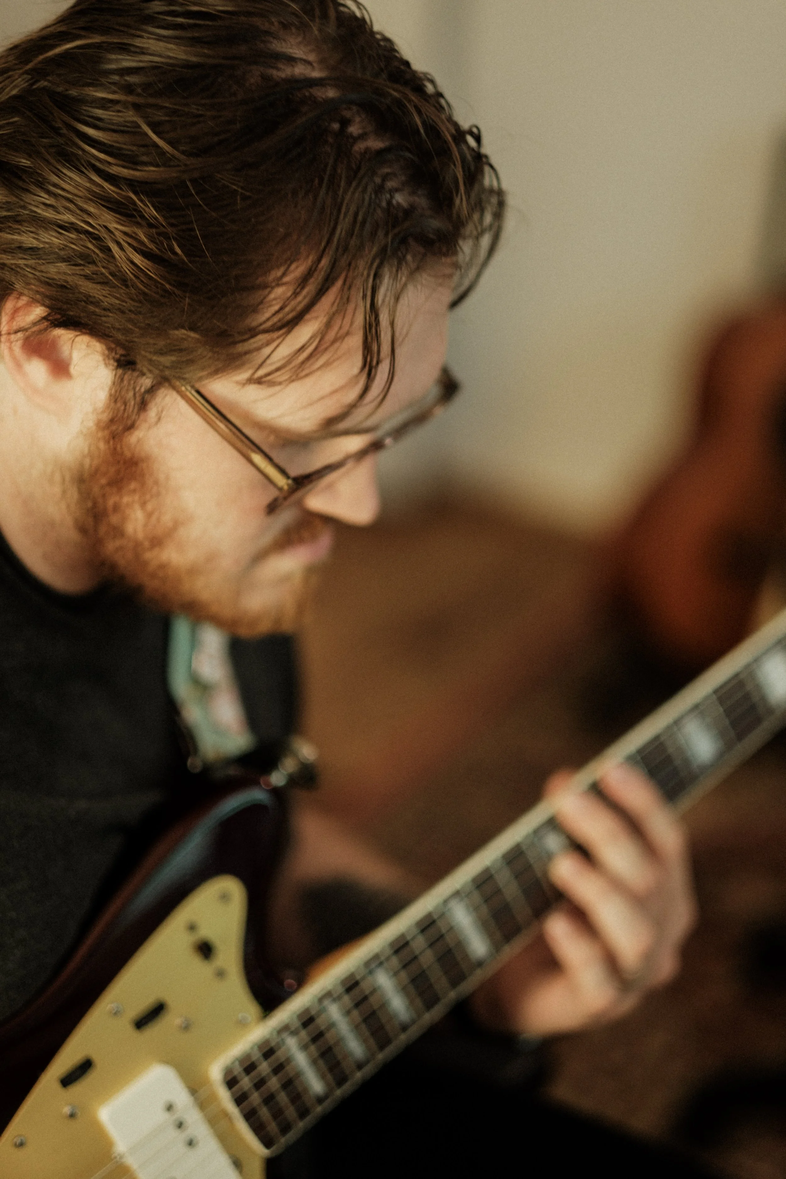 A man with glasses and red hair playing an electric guitar.