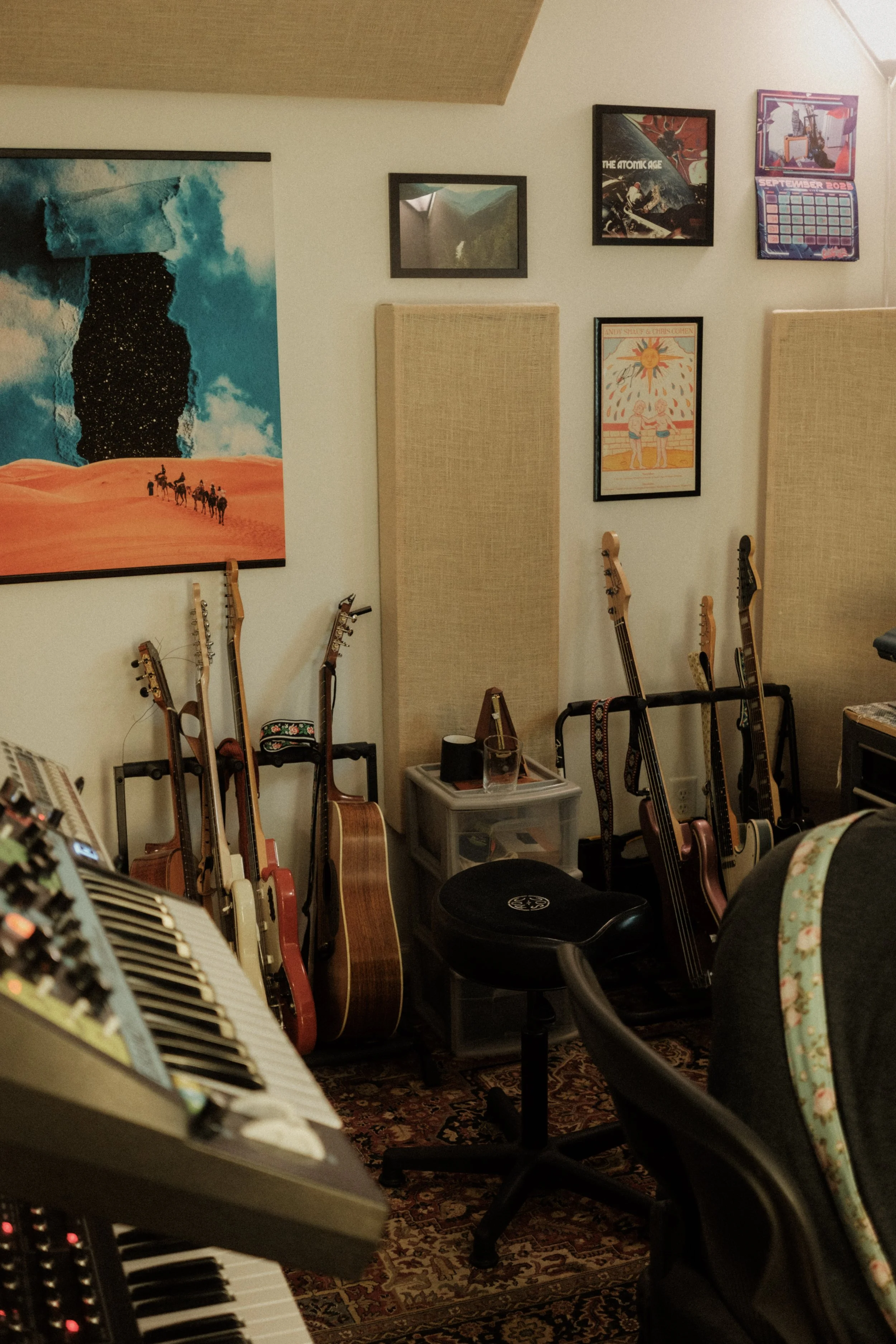 A music room with multiple guitars resting on stands, framed artwork on the wall, and a keyboard in the foreground.