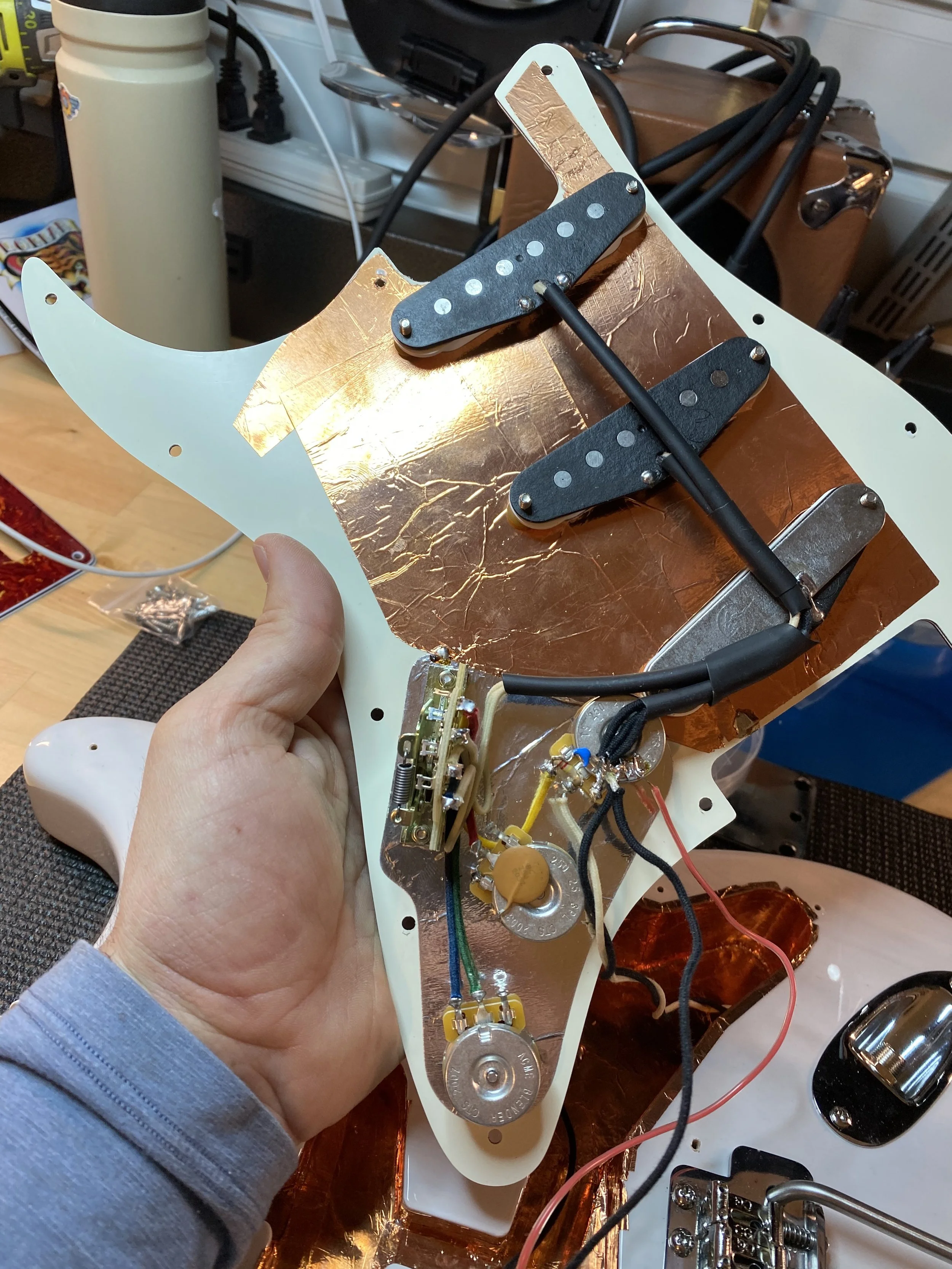 Close-up of the underside of a partially assembled electric guitar body, showing wiring, pickups, and shielding copper foil.
