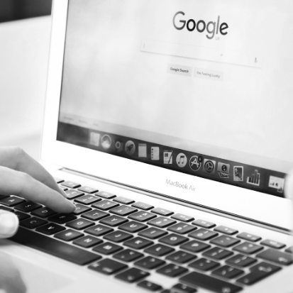 Close-up of a person's hand typing on a MacBook Air keyboard with a Google search page on the screen.